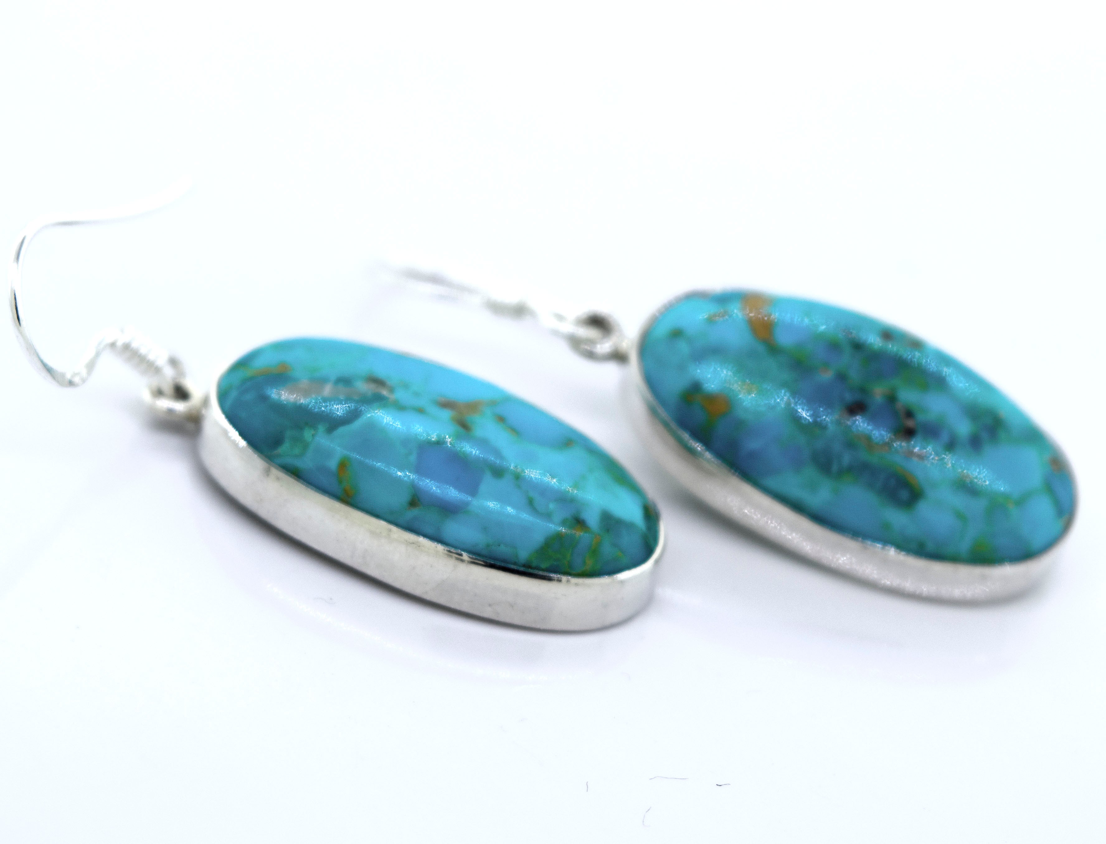 A pair of Beautiful Oval Shape Composite Turquoise Earrings by Super Silver on a white surface.