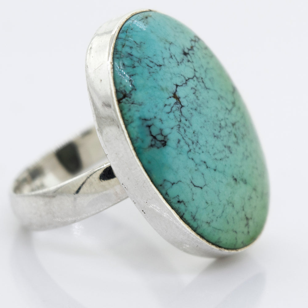 A unique Super Silver Oval Natural Turquoise Ring with a sterling silver setting on a white surface.