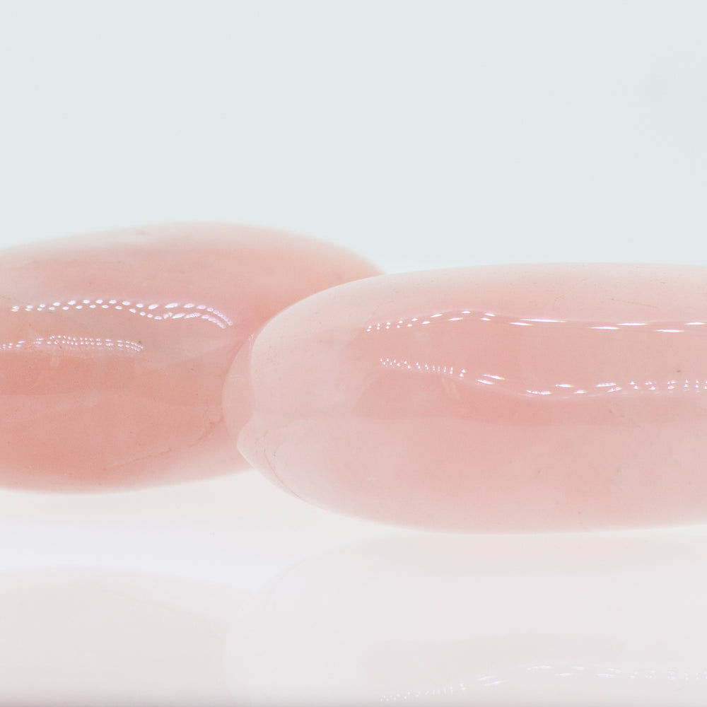 Two Rose Quartz Worry Stones on a white surface.