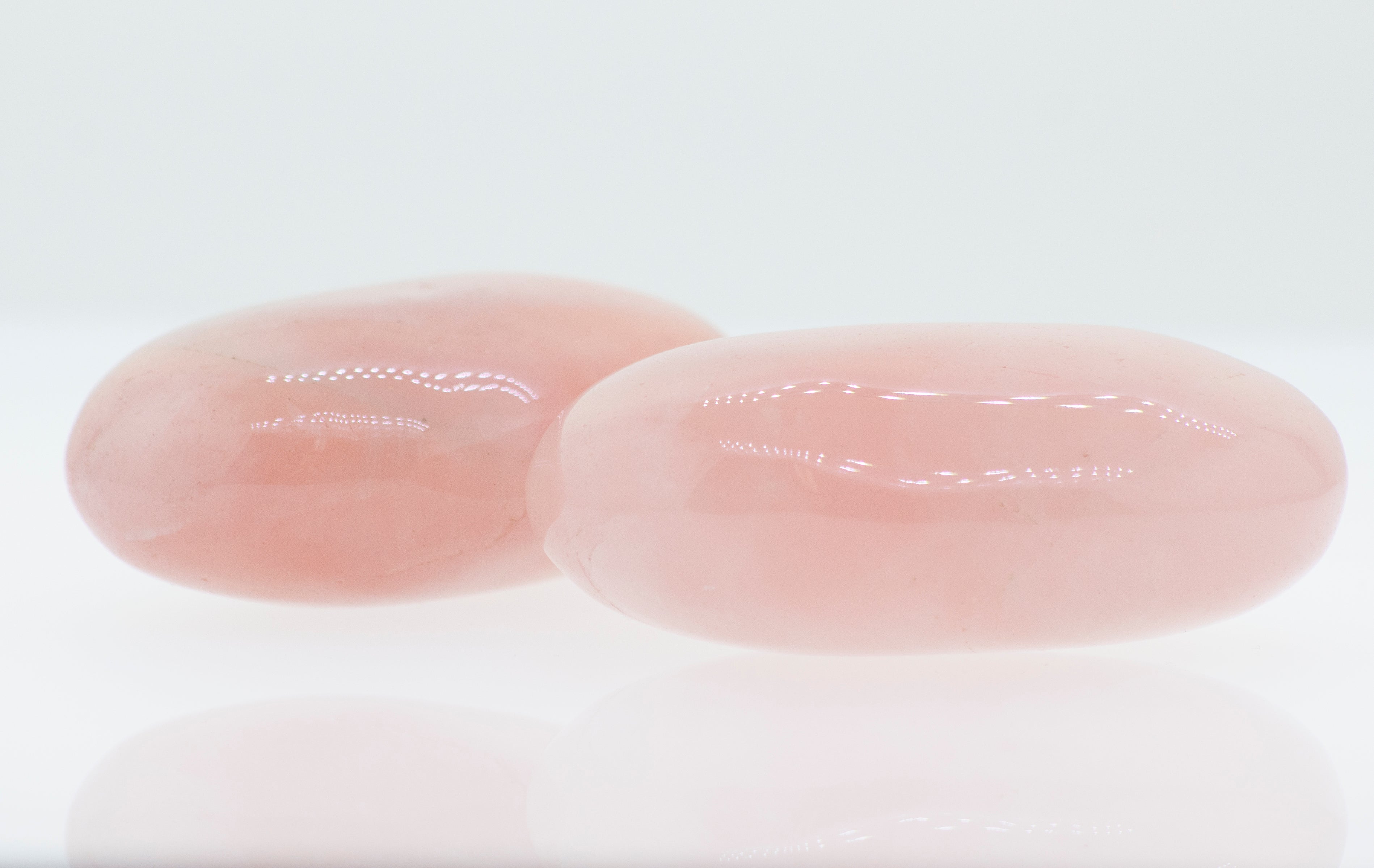 Two Rose Quartz Worry Stones on a white surface.
