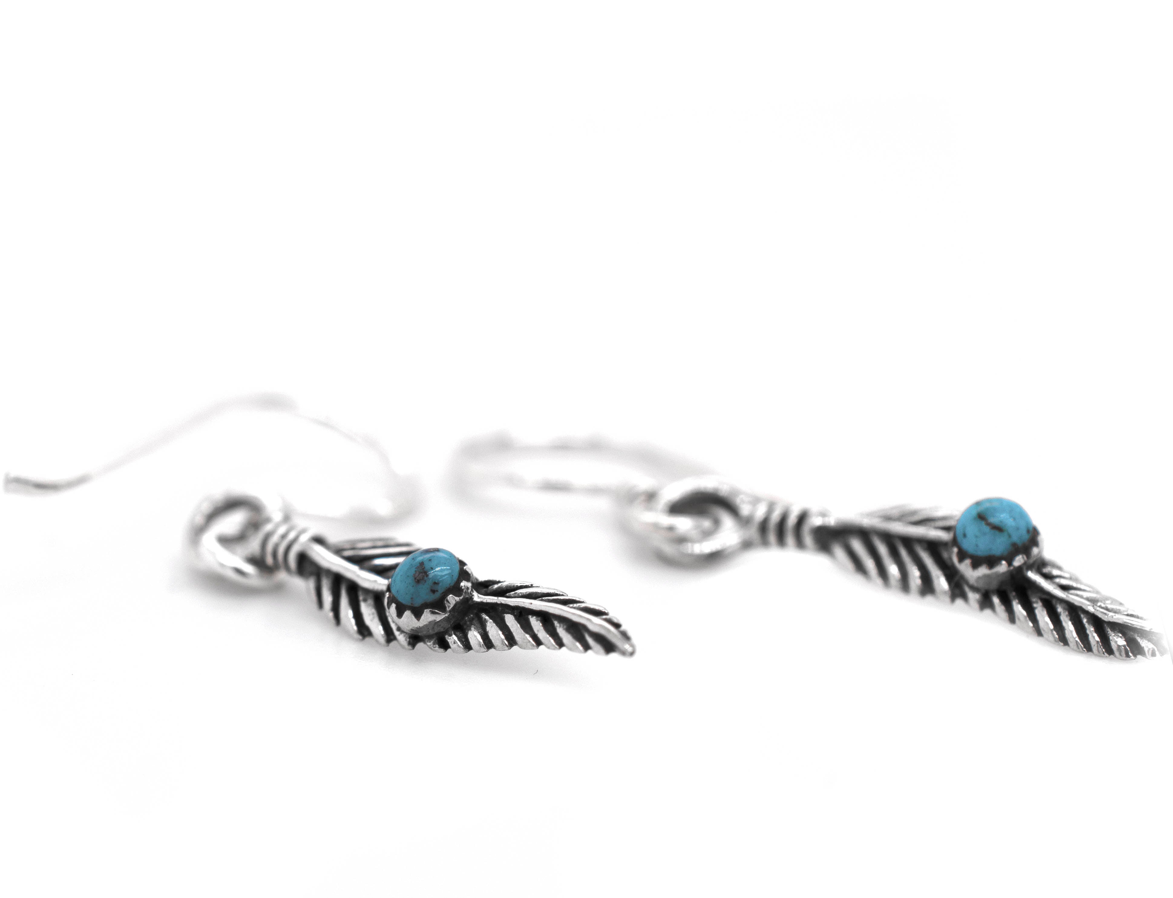 A pair of Super Silver delicate feather earrings adorned with vibrant turquoise stones.