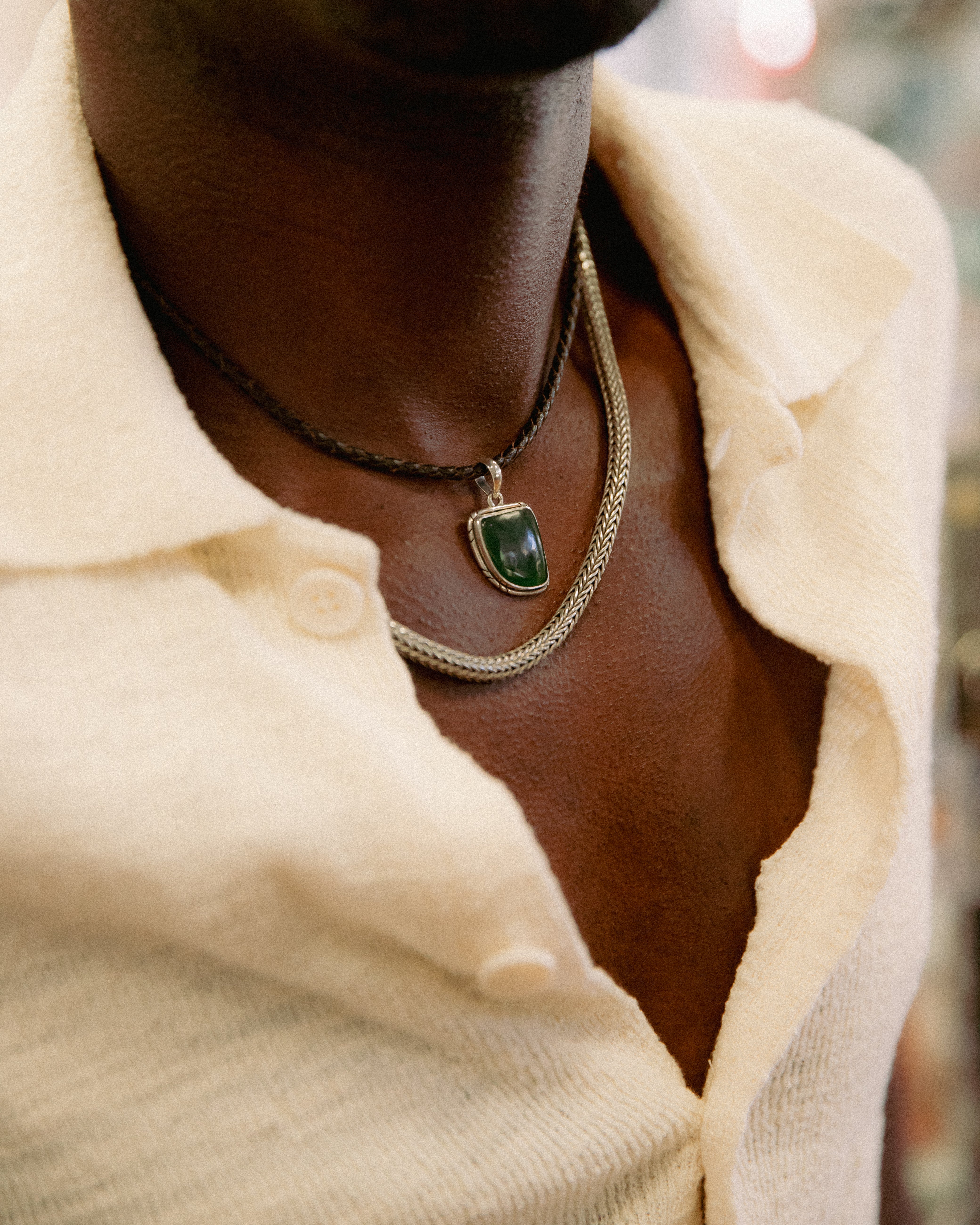 A man in a light shirt sits and smiles in front of glass display cases filled with jewelry and necklaces.