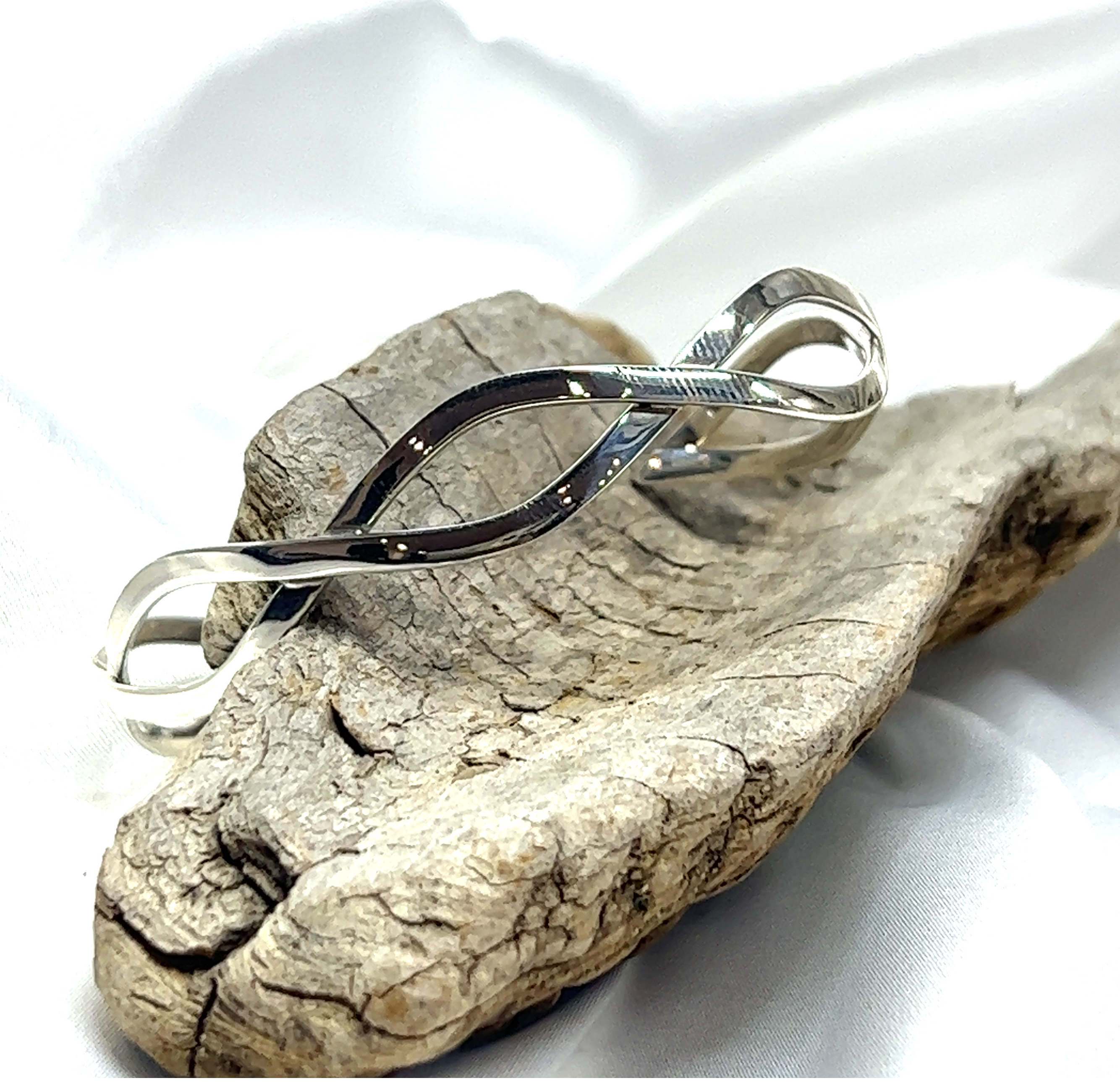 A Stylish Twisted Silver Cuff bracelet from the Super Silver brand, with a twisting pattern, sitting on top of a piece of wood.