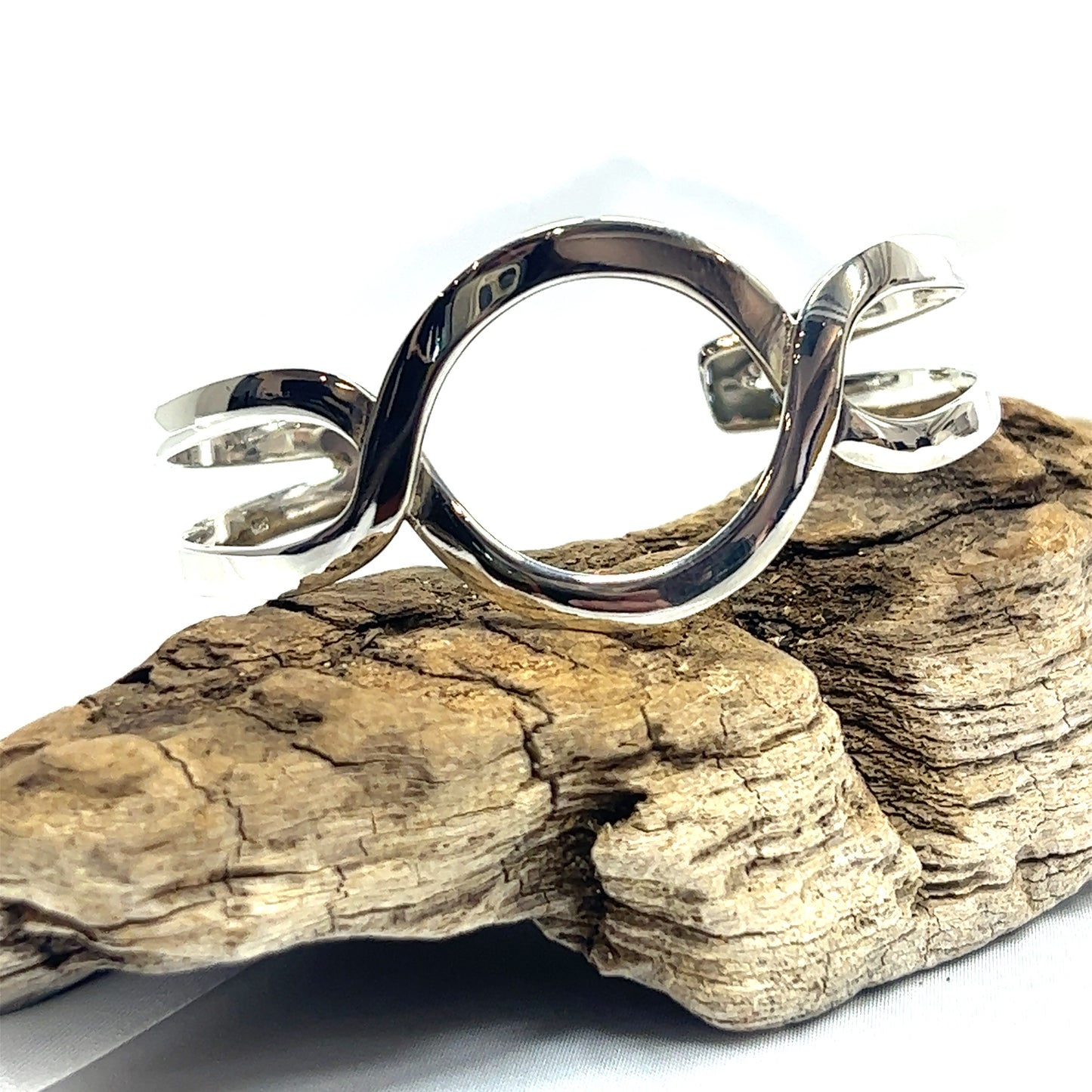 A Trendy Twisted Cuff with Circle Design bracelet from Super Silver, adding a touch of boho chic, resting on a piece of wood.