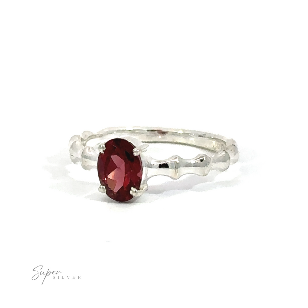 
                  
                    Pronged Oval Gemstone Ring with Textured Band with a central red gemstone flanked by two sparkling gemstones on a white background.
                  
                