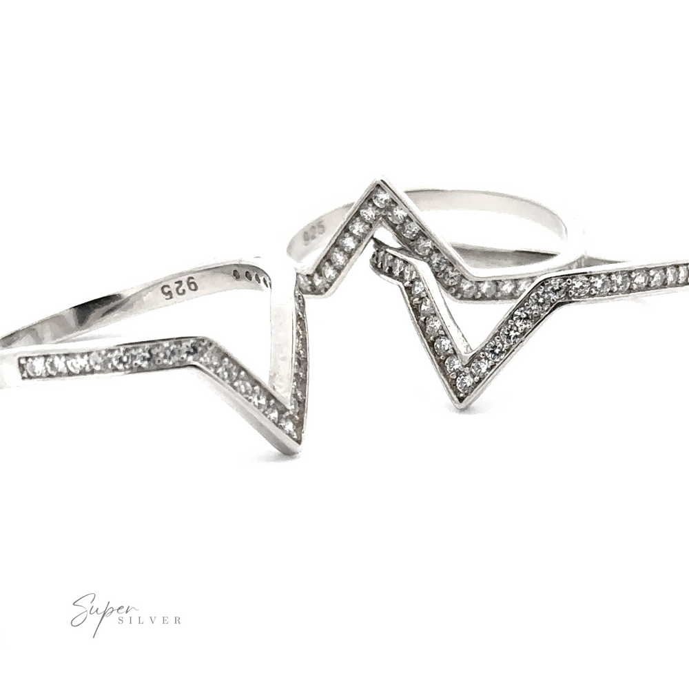 Two silver rings with zig-zag designs, each encrusted with small diamonds in a channel setting, are placed side by side against a white background. The rings have "925" engraving indicating sterling silver and "Channel Set Cubic Zirconia Chevron Ring" text is also visible. Their Rhodium Plated .925 Sterling Silver adds an extra touch of elegance.