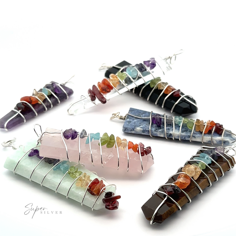 A set of seven Stone Slab Wire-Wrapped Chakra Pendants, beautifully arranged in a circle on a white surface. Each pendant showcases chakra stones meticulously placed along the wire.