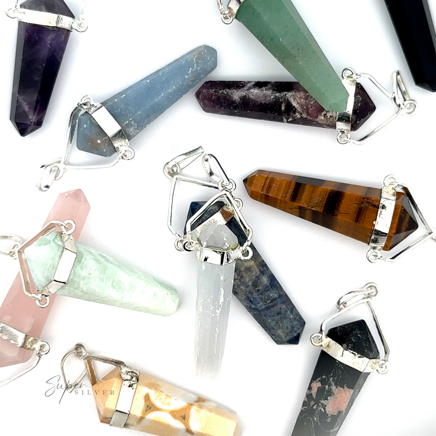Raw Stone Swivel Pendant with silver-plated settings are displayed on a white surface, featuring various colors and types such as amethyst, tiger's eye, and rose quartz. In the background, a raw stone obelisk adds a touch of natural elegance to the scene.
