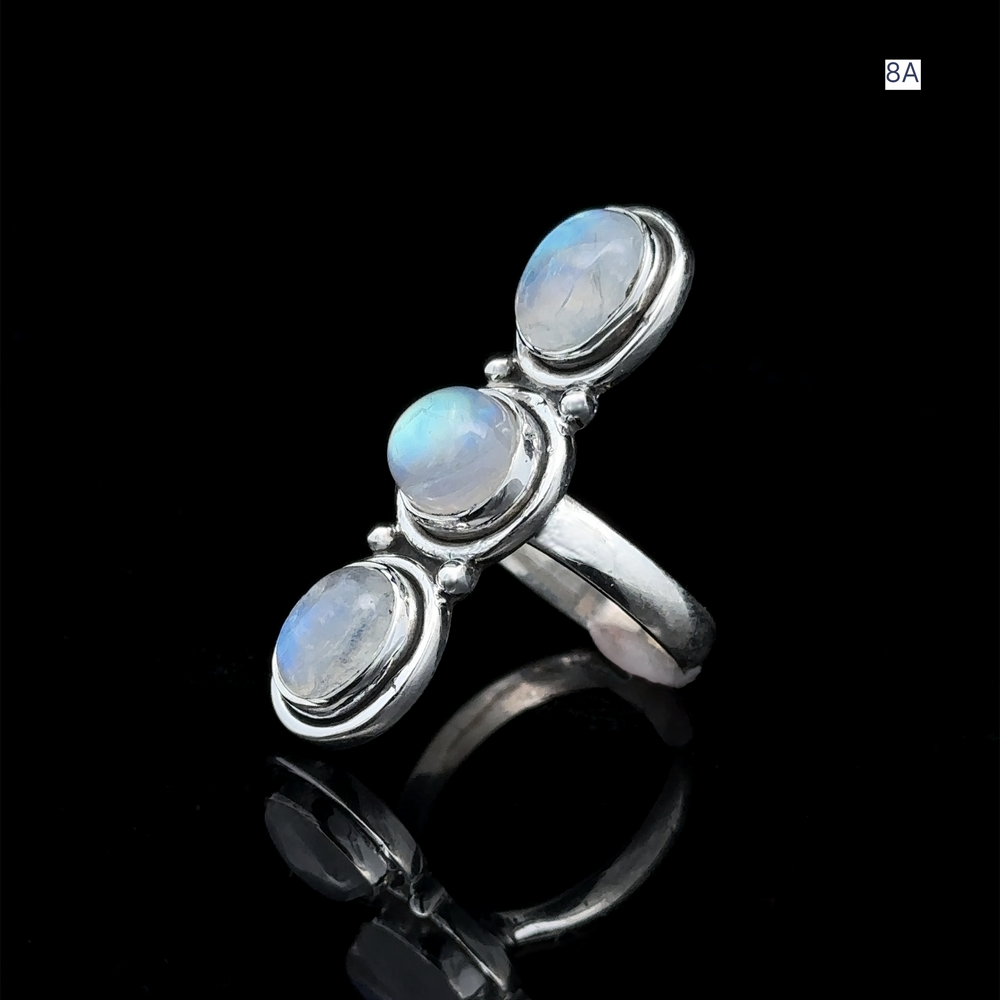 
                  
                    Triple Moonstone Ring made of sterling silver, adorned with three round blue gemstones, is elegantly showcased on a reflective black surface, exuding goddess energy.
                  
                