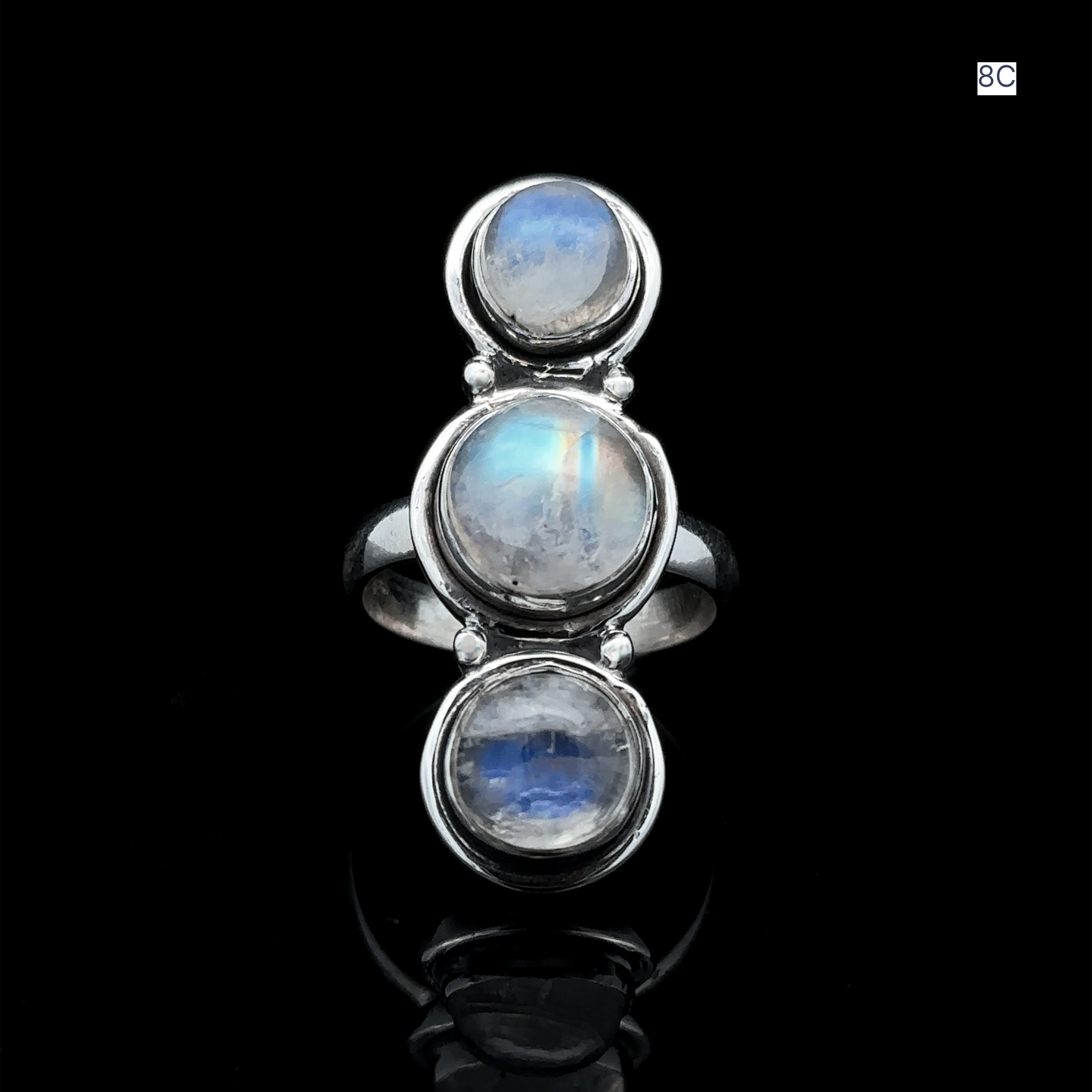 
                  
                    The Triple Moonstone Ring, crafted from sterling silver and featuring three round moonstone settings, exudes goddess energy as it gleams against a black background.
                  
                