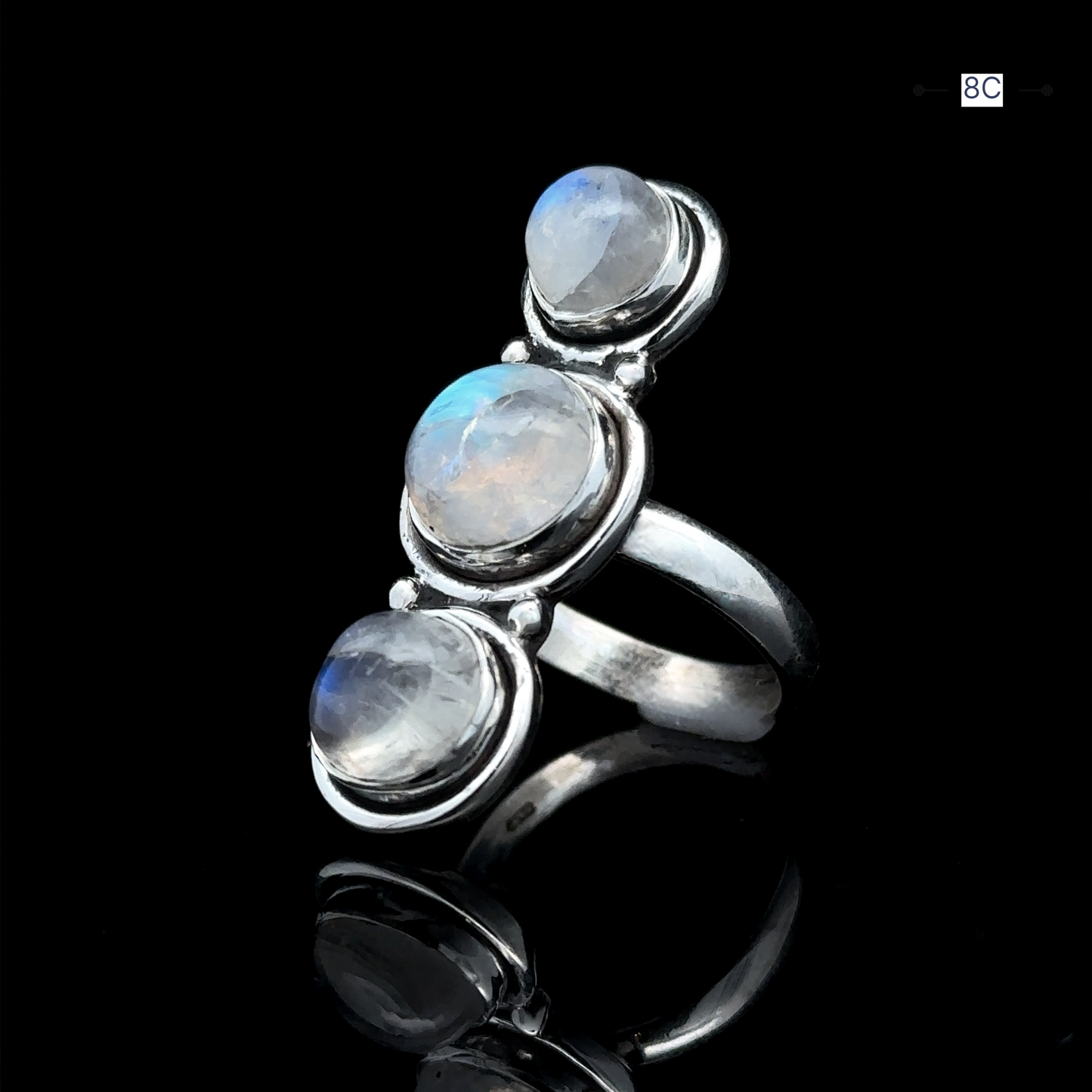 
                  
                    The Triple Moonstone Ring, crafted in sterling silver and adorned with three round moonstone gems, exudes goddess energy against a black background.
                  
                