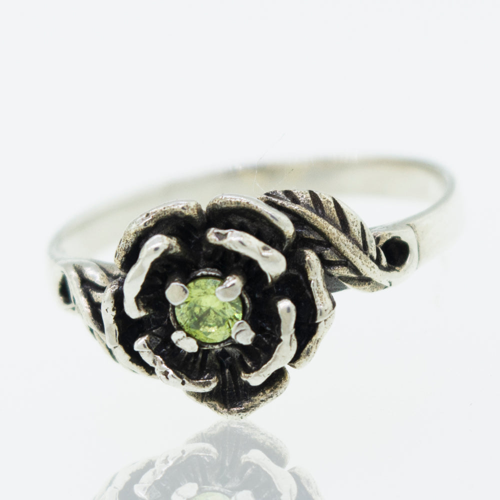 
                  
                    Rose Ring With Cubic Zirconia Stone featuring a flower design with a small green gemstone at the center.
                  
                