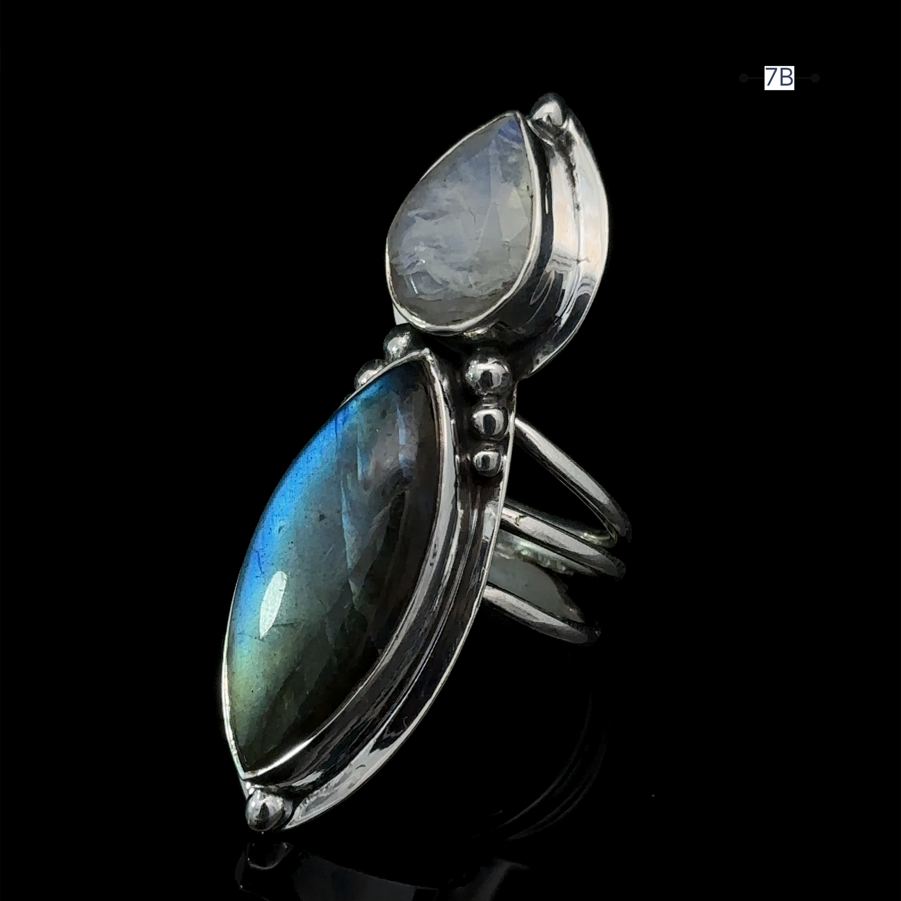 Introducing the Heavy Labradorite And Moonstone Ring—a bold silver statement ring showcasing an elongated blue labradorite gemstone paired with a smaller, translucent moonstone against a black background.