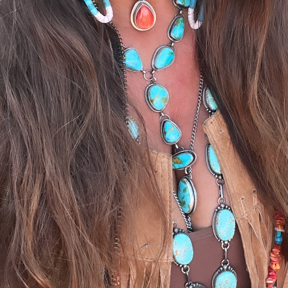 
                  
                    A person wearing a fringed tan leather jacket, a brown top, and layered turquoise jewelry crafted by Native American artisans, including necklaces, earrings, and a Wrap Around Spiny Oyster Shell Choker Necklace.
                  
                