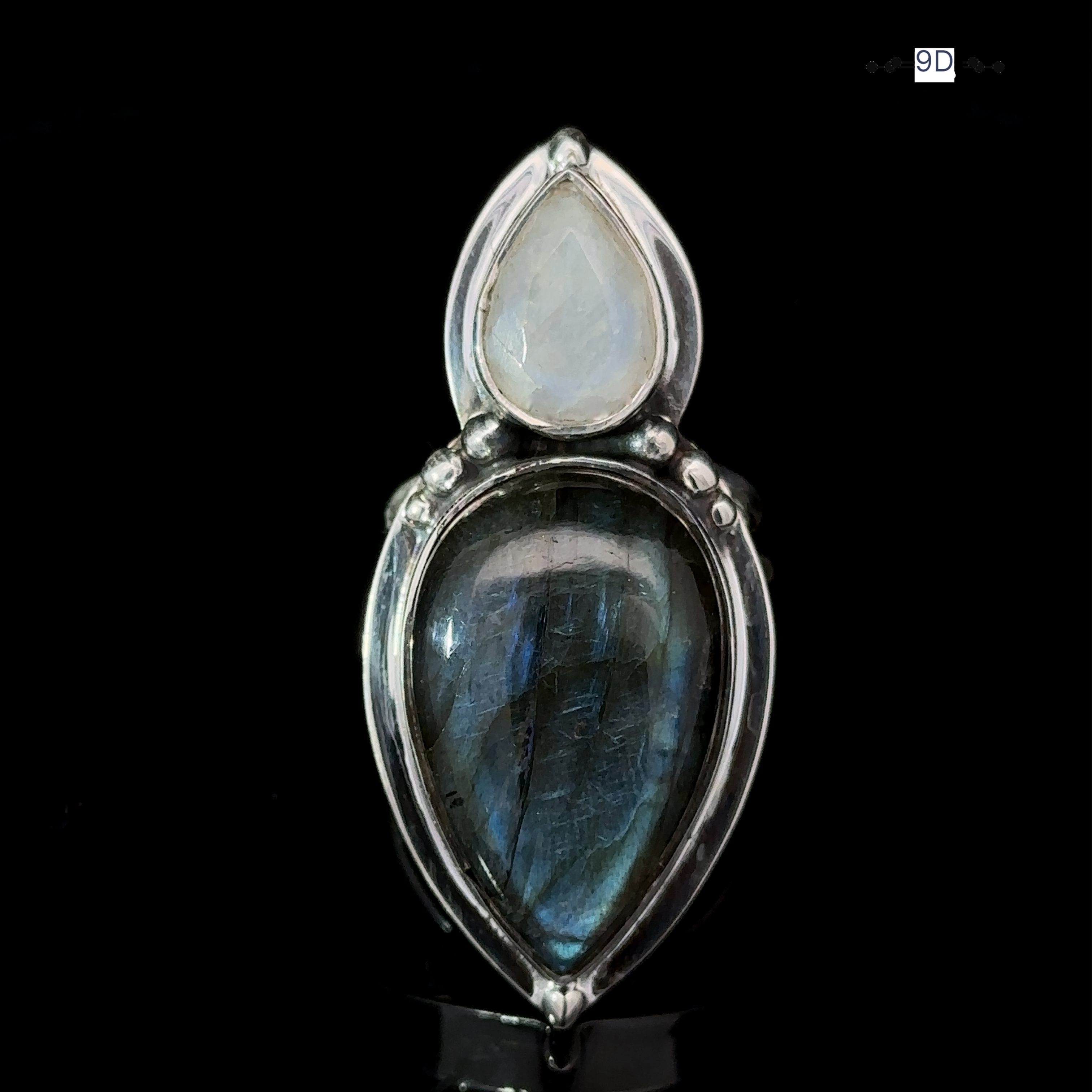 Introducing the Heavy Labradorite and Moonstone Ring, a striking silver piece showcasing two teardrop-shaped stones: one white moonstone and one dark iridescent blue labradorite, beautifully set against a sleek black background.