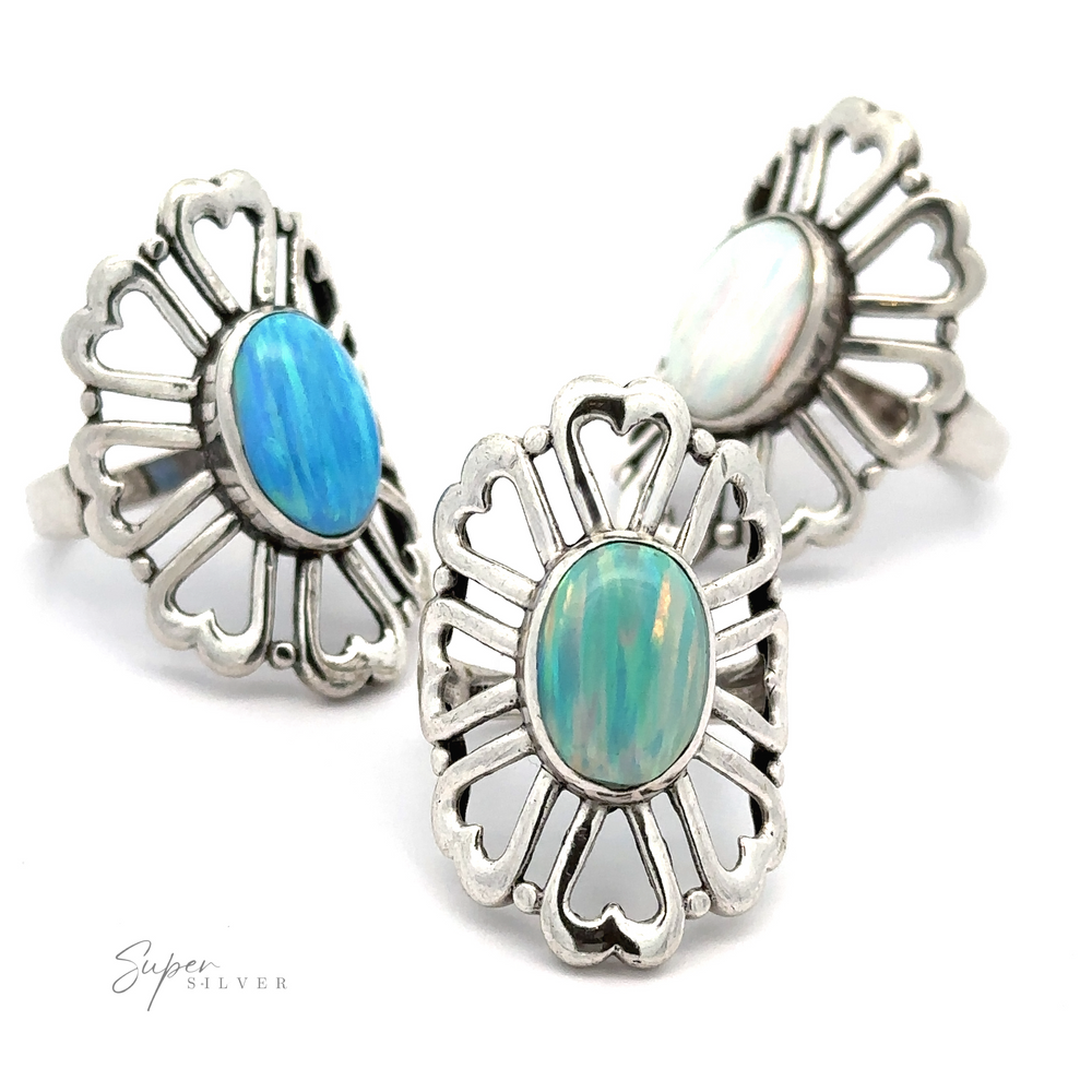 Three ornate sterling silver American Made Opal Flower Rings with Heart Shaped Petals with oval-shaped gemstones in blue, green, and white hues, arranged on a white background. Handcrafted in America.