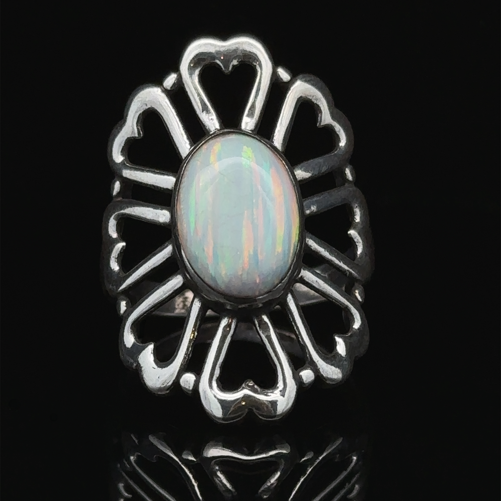 
                  
                    An American Made Opal Flower Ring with Heart Shaped Petals is set in an ornate heart-shaped design against a black background, handcrafted in America.
                  
                