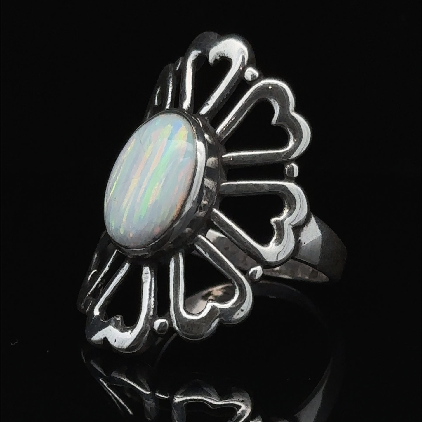 
                  
                    The American Made Opal Flower Ring with Heart Shaped Petals, featuring a central oval opal gemstone on a black background, handcrafted in America.
                  
                