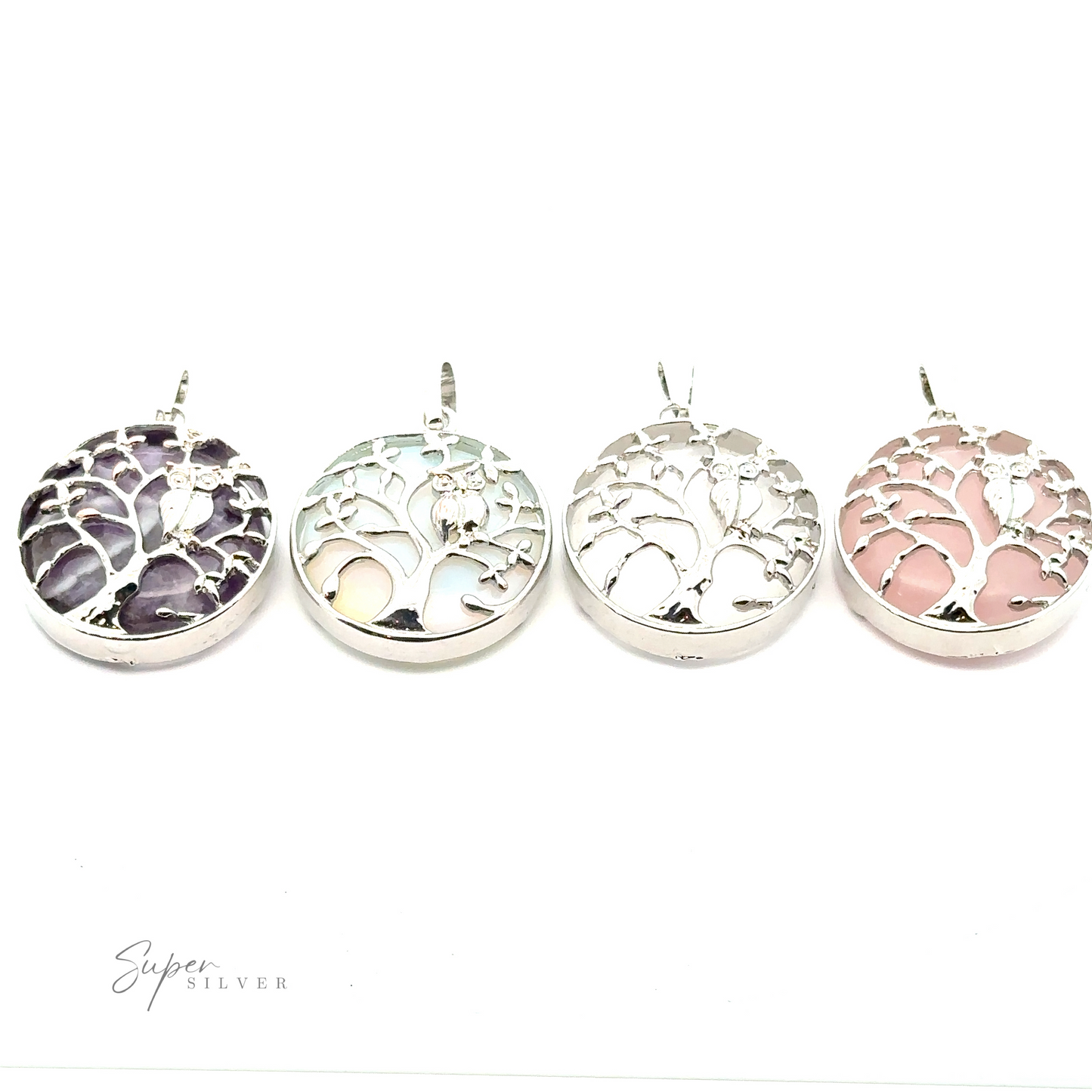 Four Owl and Tree Pendants with different colored backgrounds are displayed in a row on a white surface. The colors from left to right are blue, green, purple Amethyst, and pink. Designed with mixed metals, these pieces add an elegant touch to any outfit.