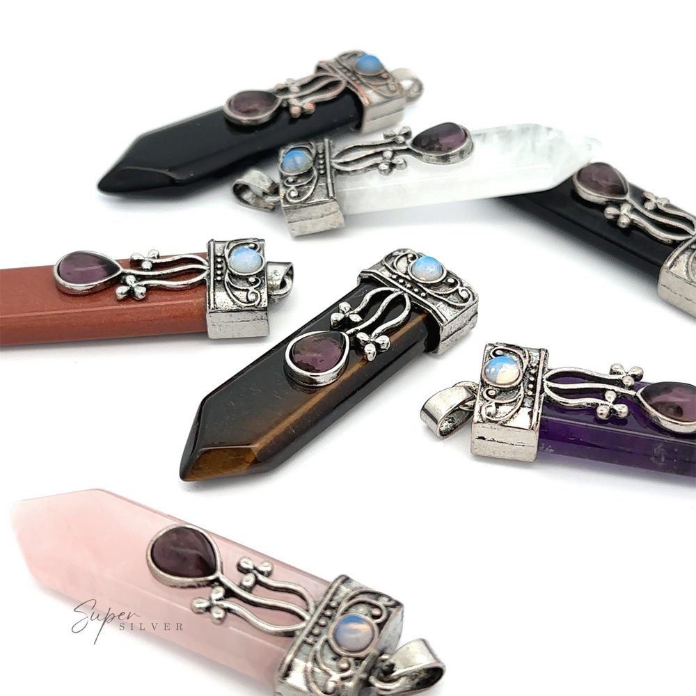 A collection of gemstone pendants, each with a metal cap and decorative design featuring small colored stones, arranged on a white surface. The Obelisk Crystal Stone Pendant showcases hues like black, white, brown, purple Amethyst, and pink Opalite.