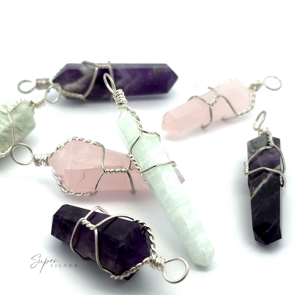 Various Wire-Wrapped Stone Pendants are displayed on a white surface. These wire-wrapped pendants feature genuine stones in shades of purple, pink, and green.