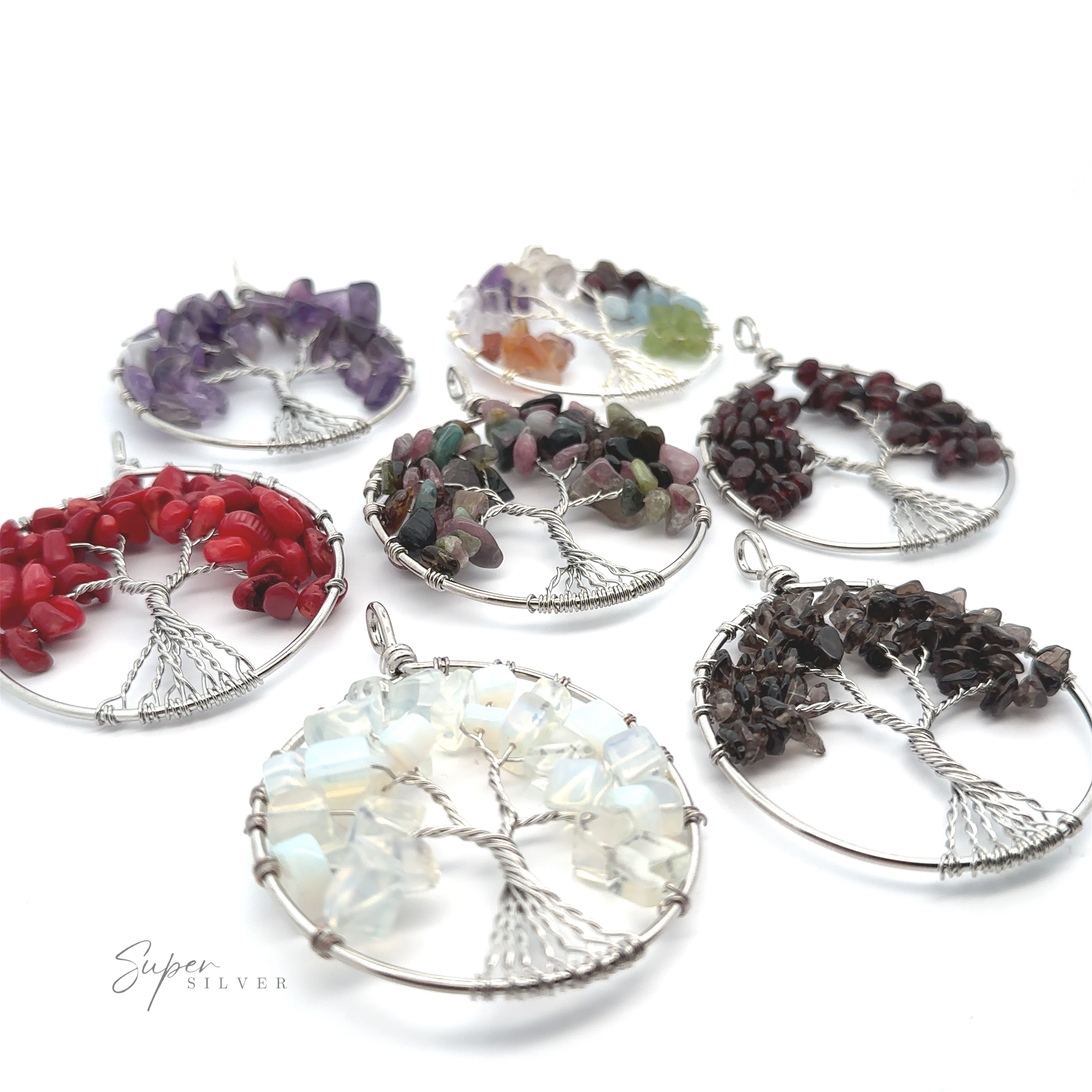 Seven Wire Wrapped Tree of Life Pendants with different colored gemstone chips, crafted from mixed metals, are arranged in a semi-circle on a white background.