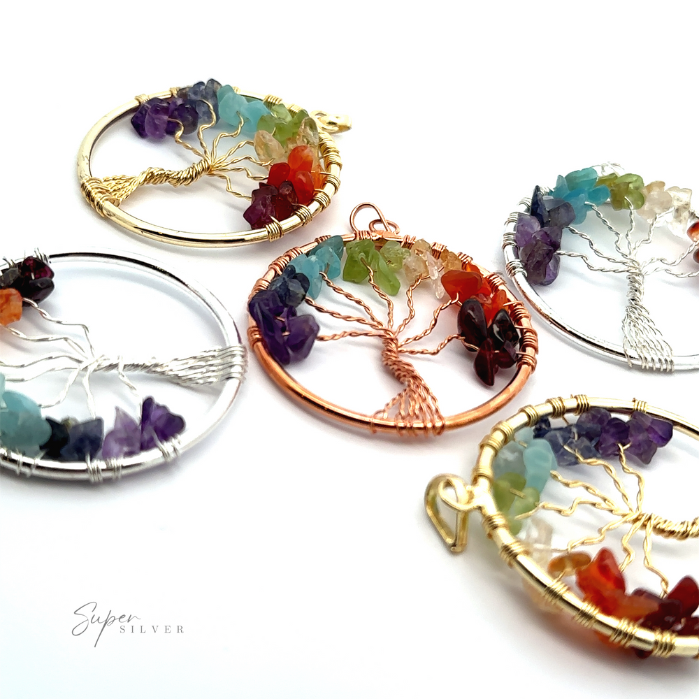 
                  
                    Five Wire-Wrapped Chakra Tree of Life Pendants featuring multicolored chakra stones are displayed on a white surface. The wire-wrapped pendants have circular frames in gold, silver, and copper tones.
                  
                