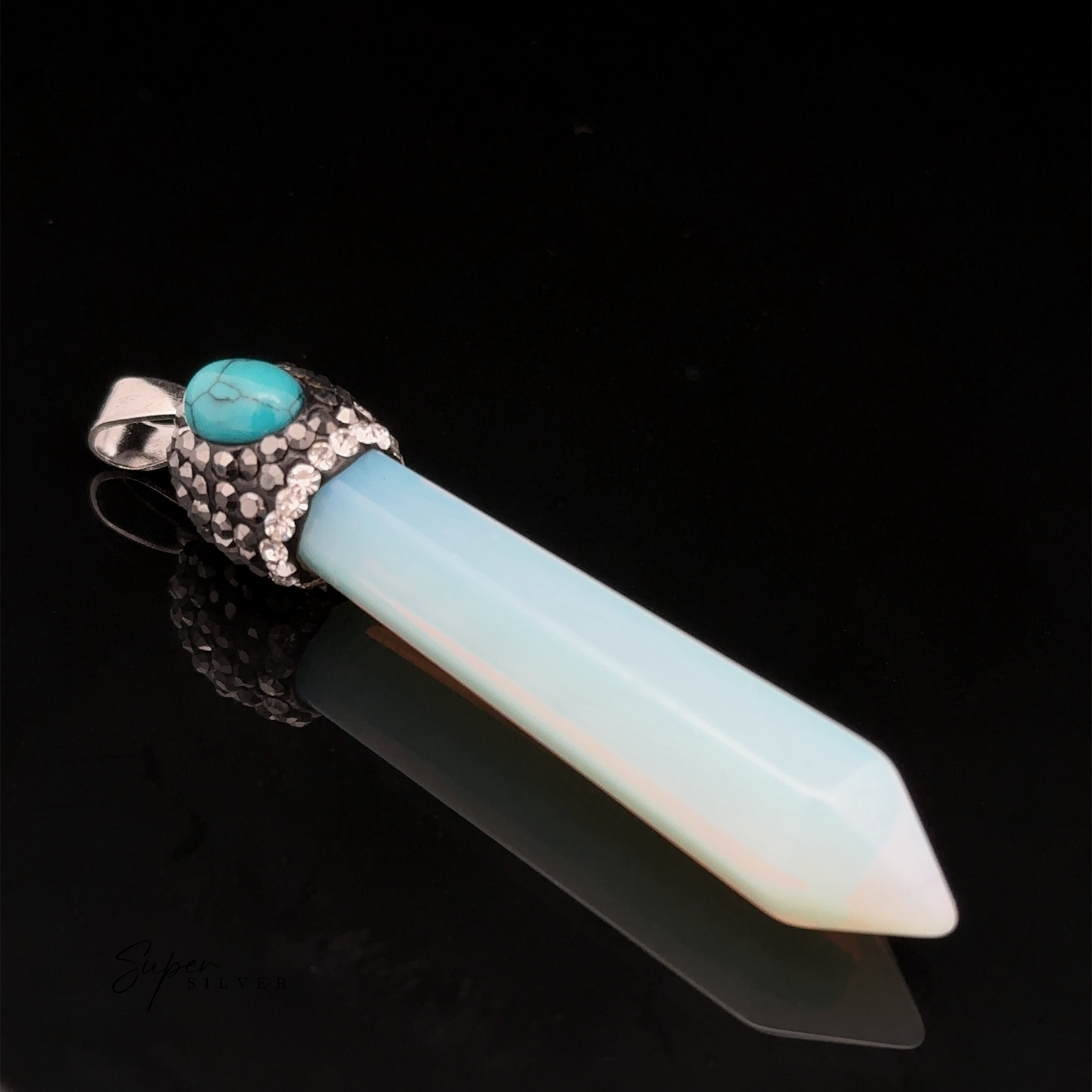 An Stone Obelisk Pendant featuring a pointed white and blue gemstone, topped with a decorative silver cap and a small turquoise stone, rests elegantly on a black background.
