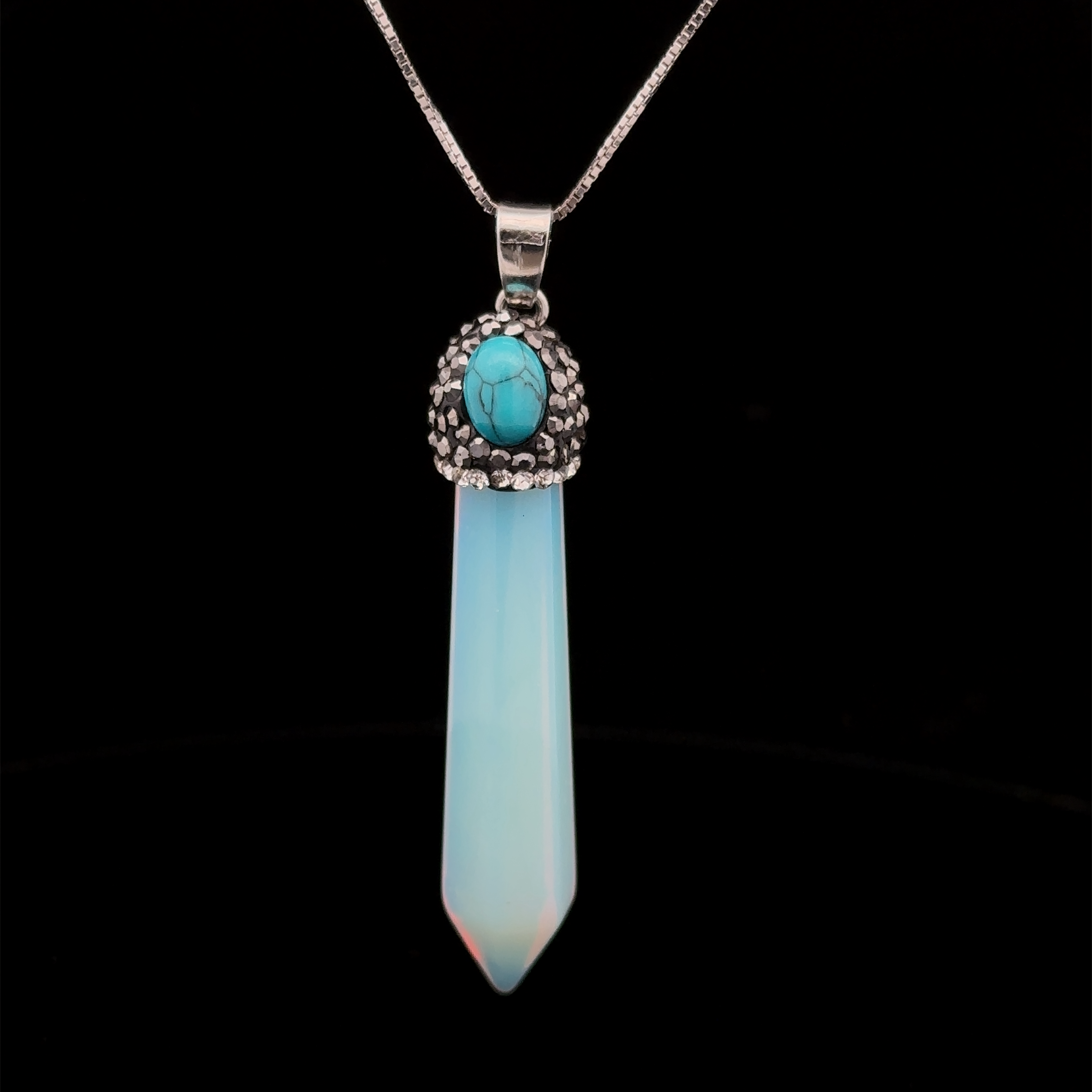 A Stone Obelisk Pendant featuring a blue, tapered stone set in a decorative, silver-toned metal holder, enhanced with hematite beads, hanging from a thin, silver-toned chain.