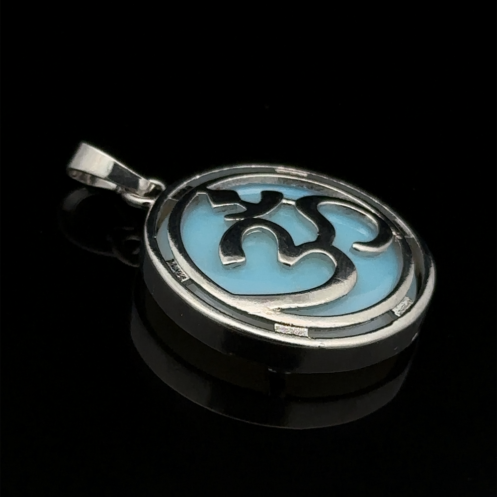 
                  
                    An Om Pendant with a silver outer design featuring a heart and swirl pattern over a light blue background, accented with mixed metals, placed against a black backdrop.
                  
                