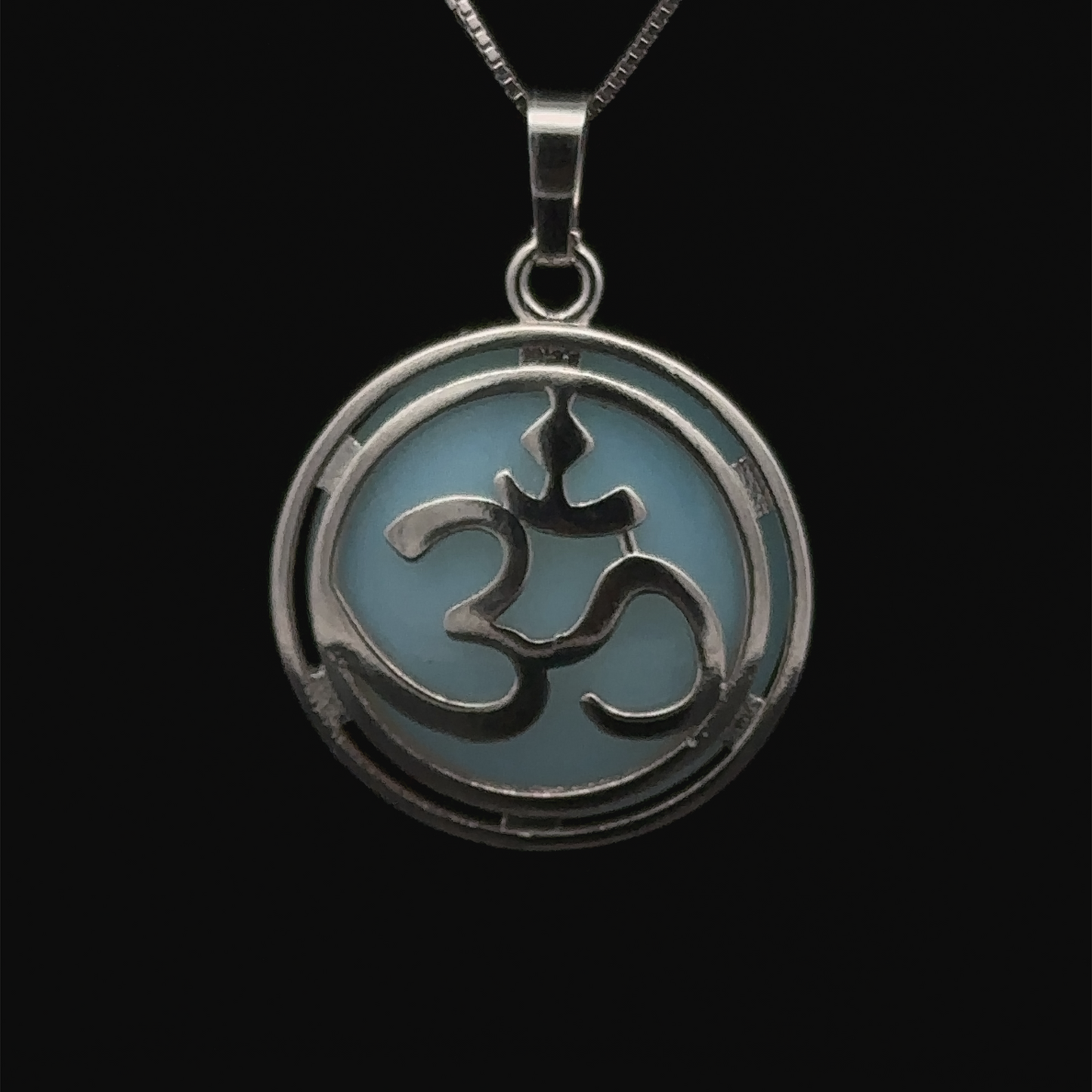 
                  
                    A round, silver-plated Om Pendant with a light blue background is hanging on a chain, accented with a touch of opalite for added elegance.
                  
                