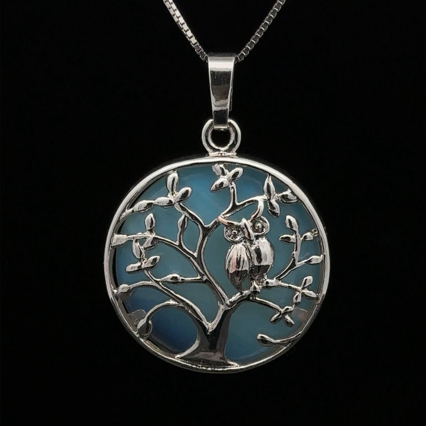 
                  
                    A silver Owl and Tree Pendant featuring a detailed tree with Amethyst accents and two owls perched on a branch against a blue background.
                  
                