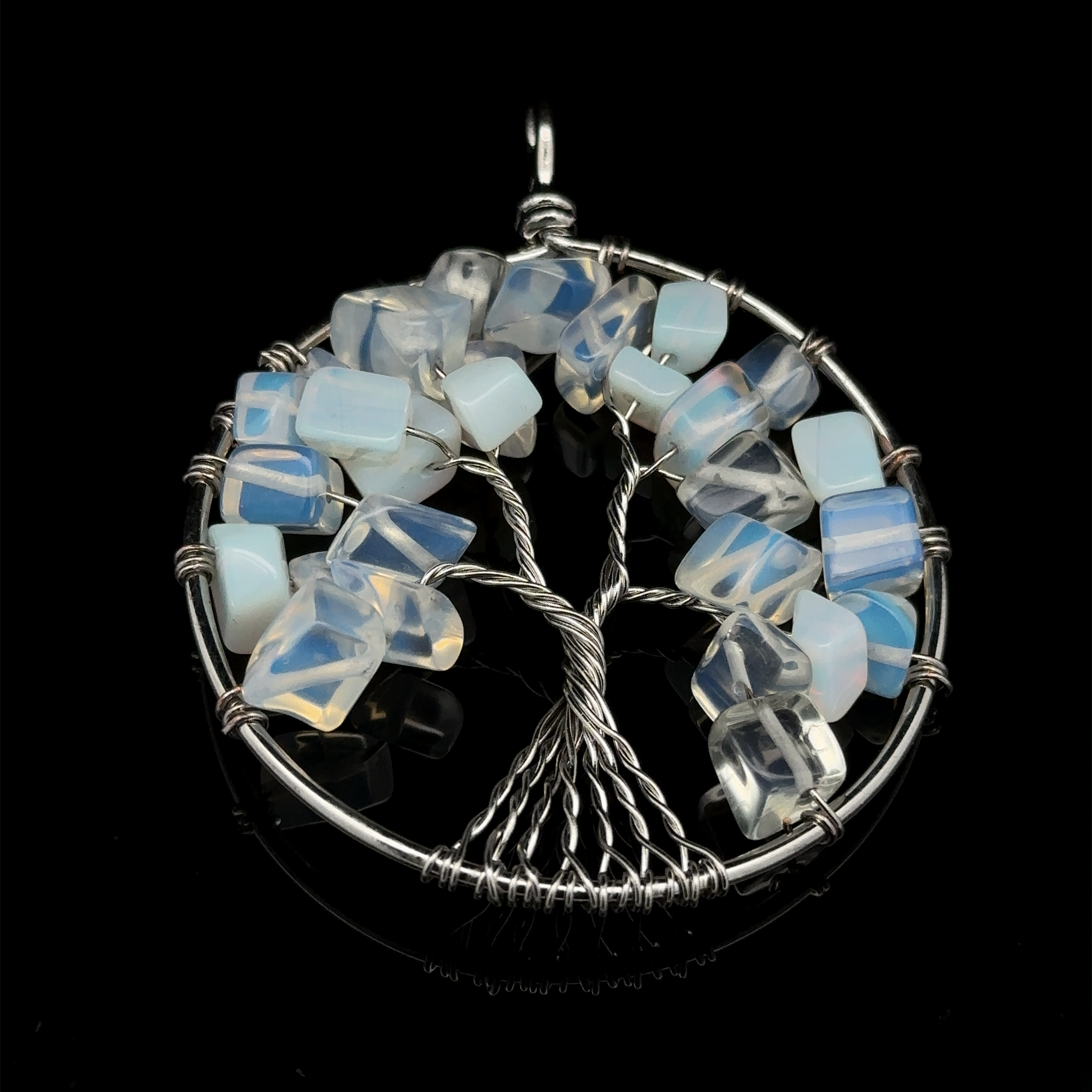 A stunning Wire Wrapped Tree of Life Pendant showcases a silver wire design adorned with blue and white gemstones embedded in the branches, all set against a sleek black background. The piece beautifully integrates mixed metals to create a striking contrast.