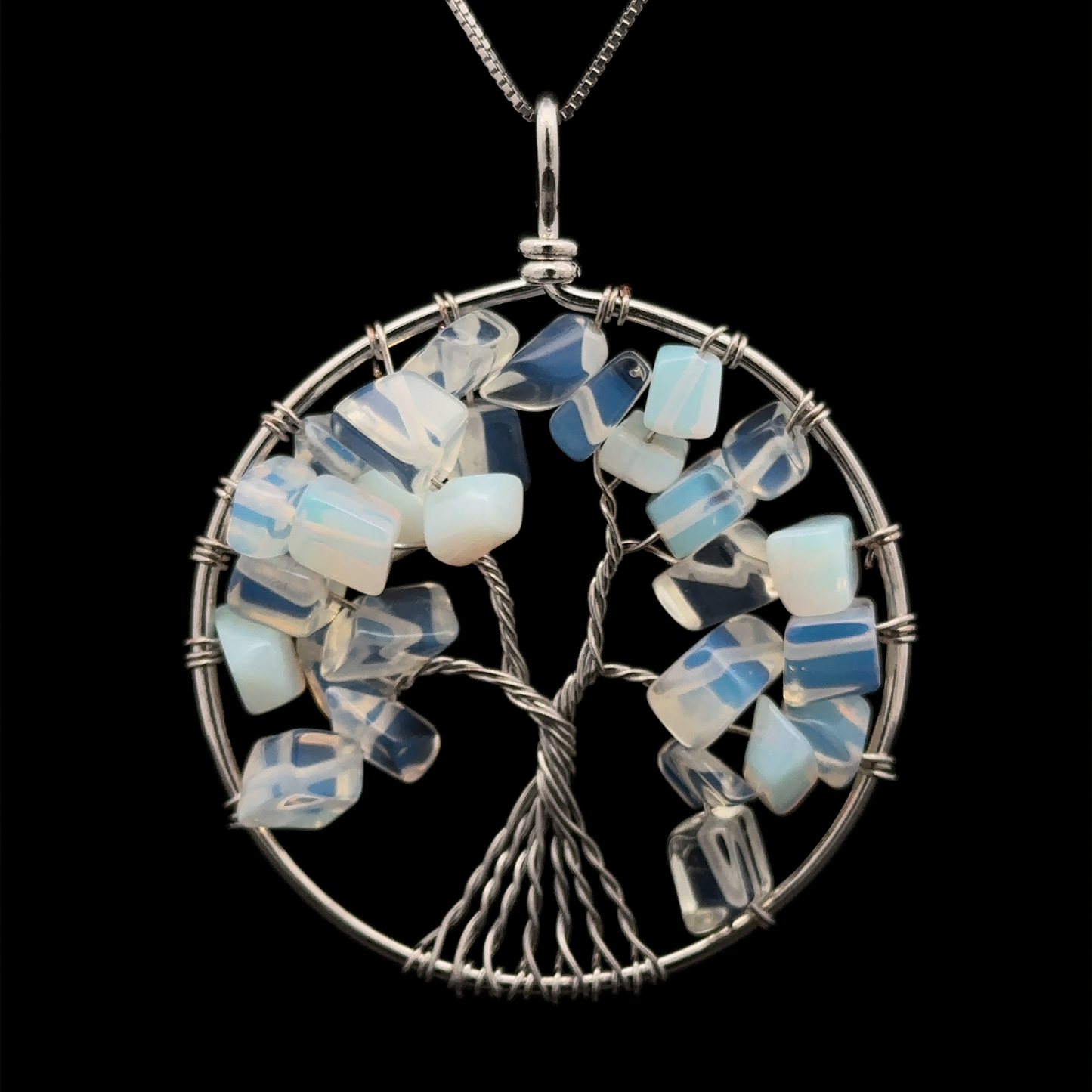 
                  
                    A Wire Wrapped Tree of Life Pendant featuring a tree made from twisted wire with blue and white gemstone chips, set in a circular mixed metals frame on a dark background.
                  
                