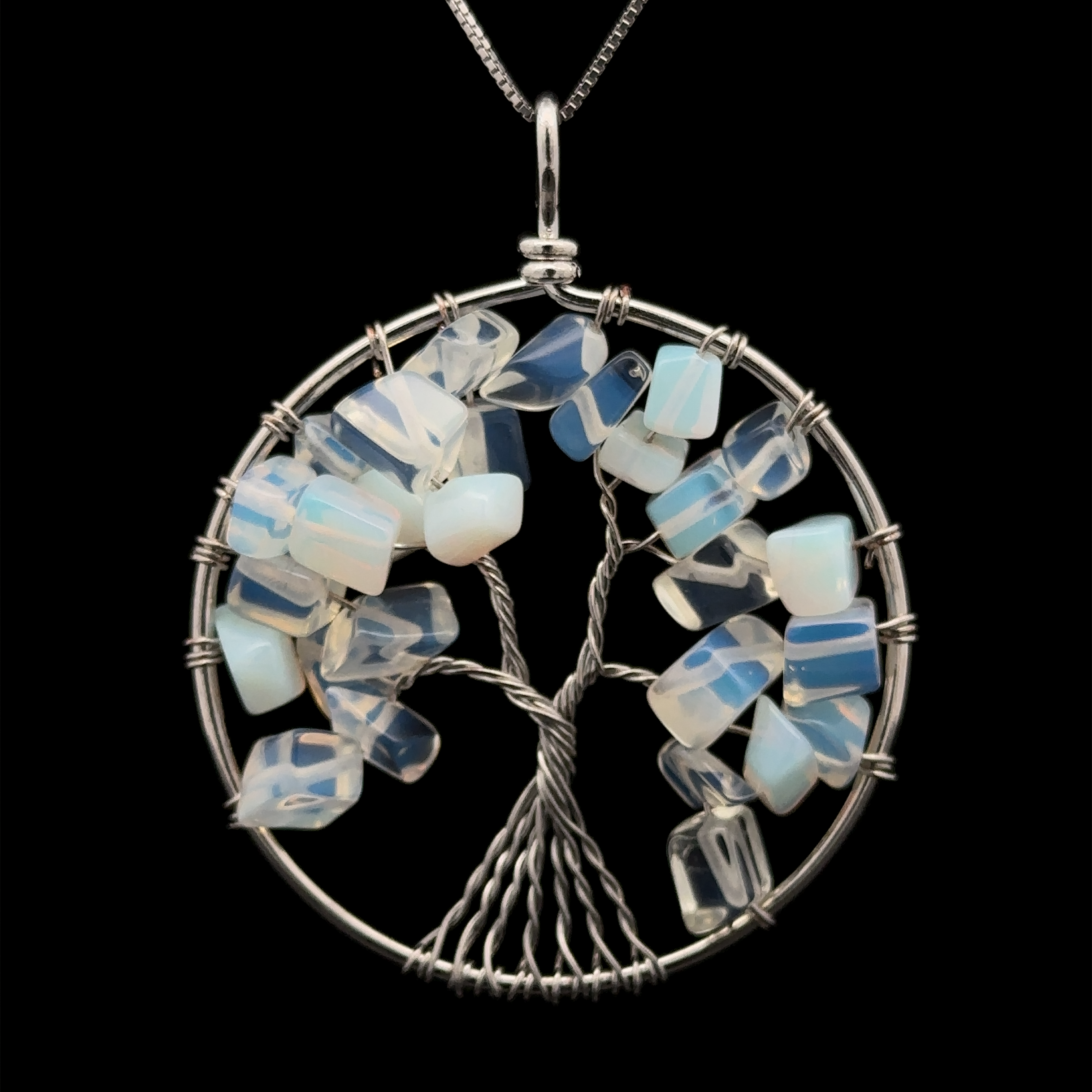 A Wire Wrapped Tree of Life Pendant featuring a tree made from twisted wire with blue and white gemstone chips, set in a circular mixed metals frame on a dark background.