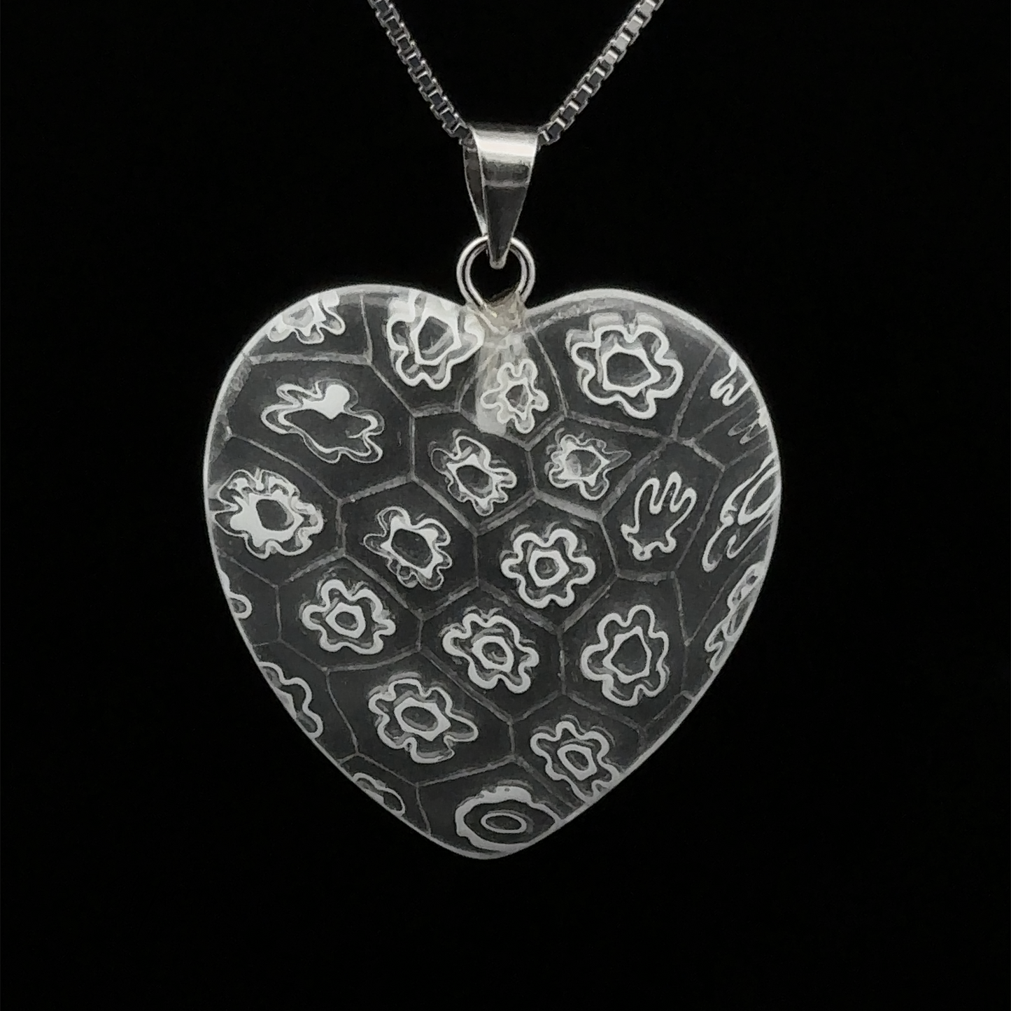 
                  
                    Heart Pendant with Flower Pattern suspended from a silver chain against a black background.
                  
                
