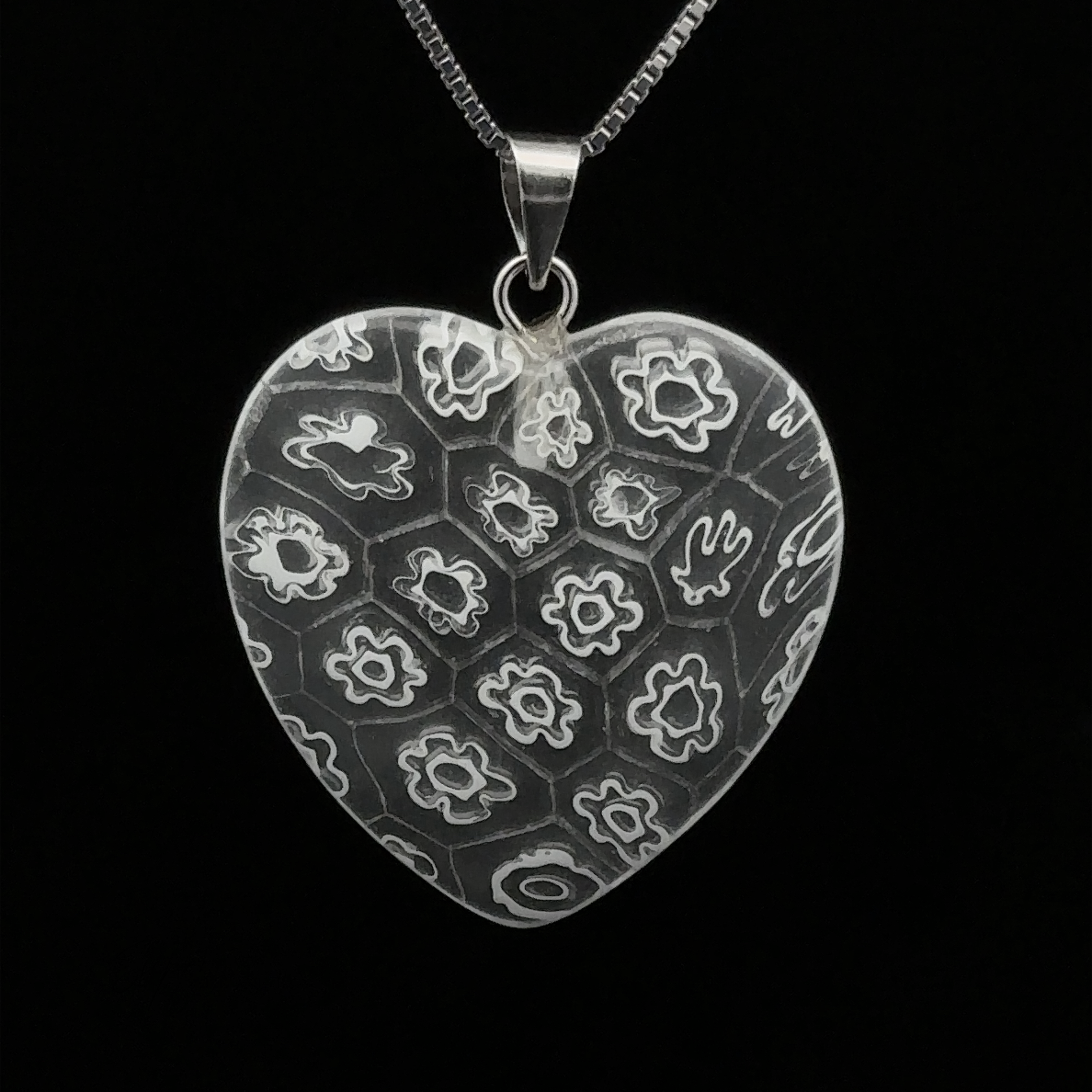Heart Pendant with Flower Pattern suspended from a silver chain against a black background.