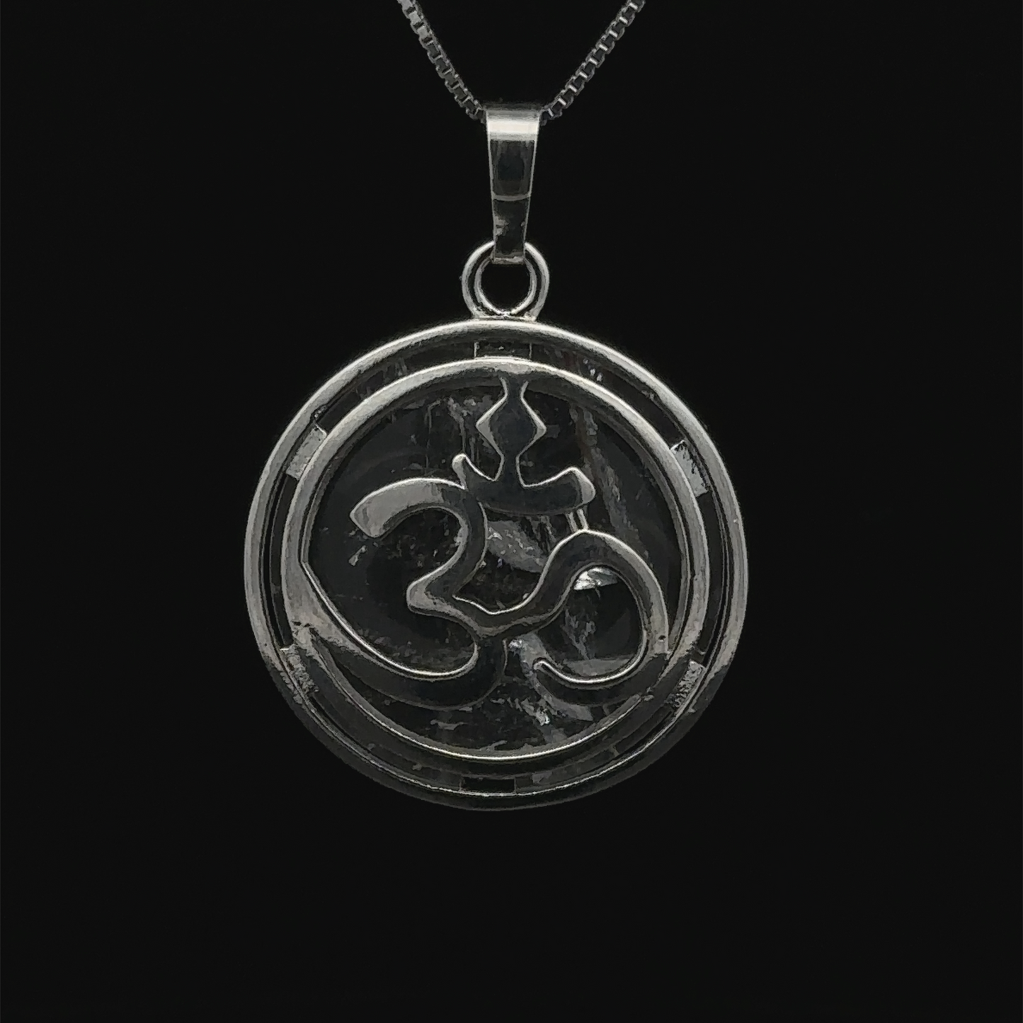 
                  
                    An Om Pendant with an intricate silver plated Om symbol at its center, set against a black background.
                  
                