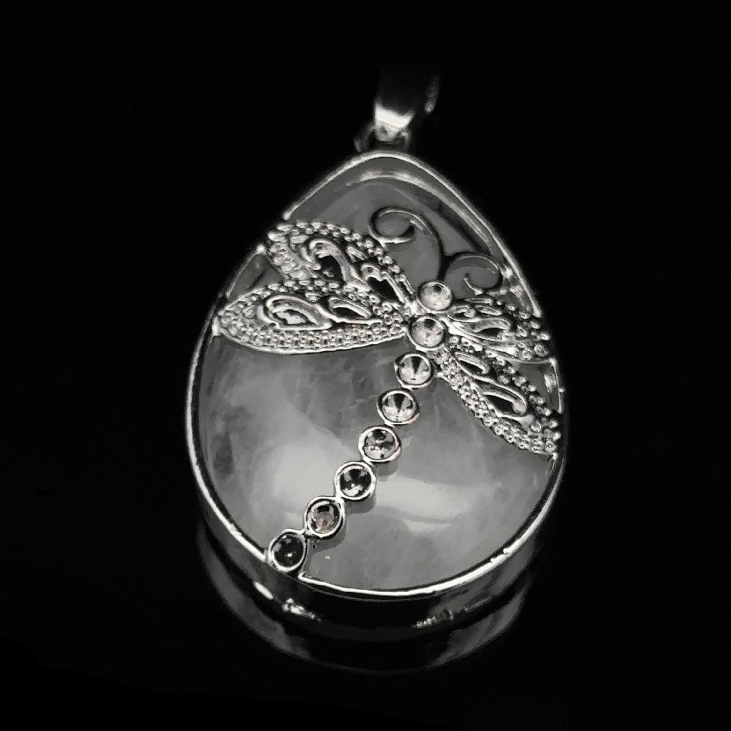 A Teardrop Stone pendant with Dragonfly embellished with small amethyst gemstones on a dark background.
