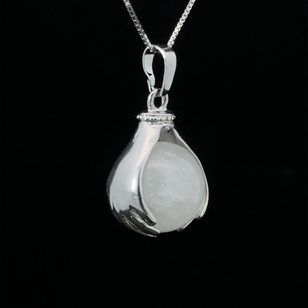 
                  
                    A Sphere Crystal Pendant features two hands delicately holding a round quartz stone. The pendant hangs from a fine silver chain against a black background.
                  
                