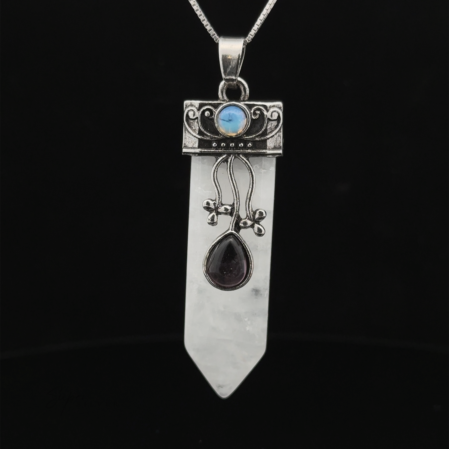 
                  
                    An Obelisk Crystal Stone Pendant with intricate silver designs features a blue gemstone, a pointed clear crystal, and a teardrop-shaped dark gem. Attached to a chain, the pendant stands out beautifully against a black background.
                  
                