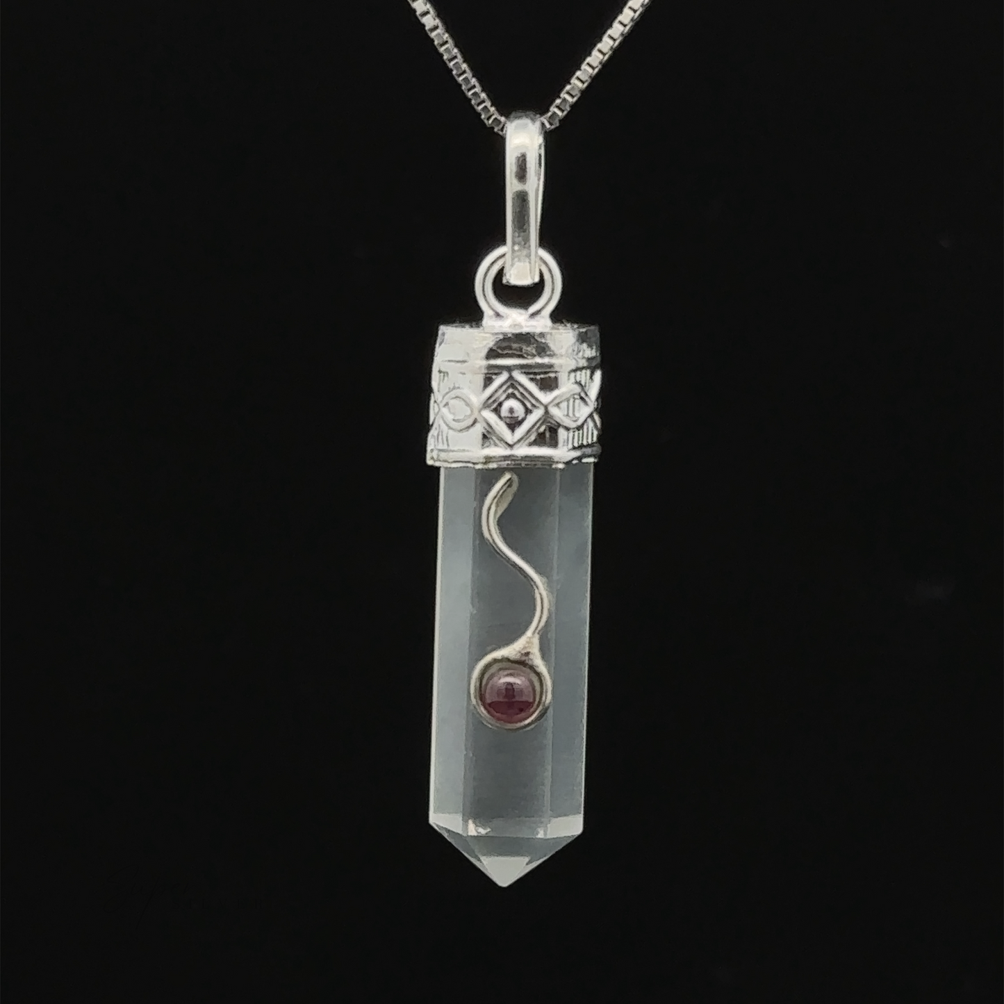 
                  
                    A clear Crystal Pendant with Decorative Bail, encased in an ornate silver cap, hangs on a delicate silver chain against a black background, showcasing exquisite garnet detail.
                  
                