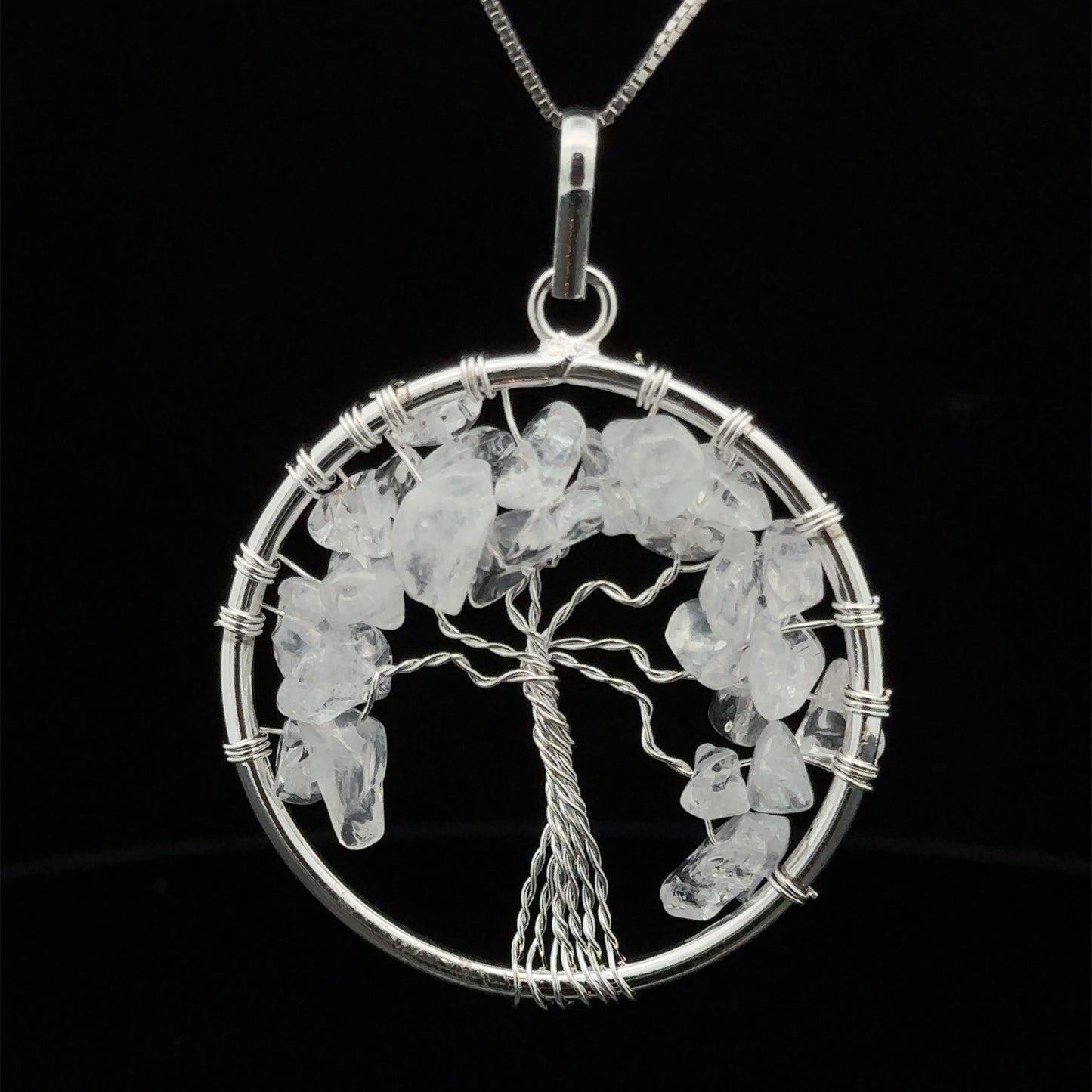 
                  
                    A round silver Wire Wrapped Tree of Life Pendant with Stones features wire-wrapped branches adorned with clear gemstones. The pendant hangs from a silver chain against a black background.
                  
                