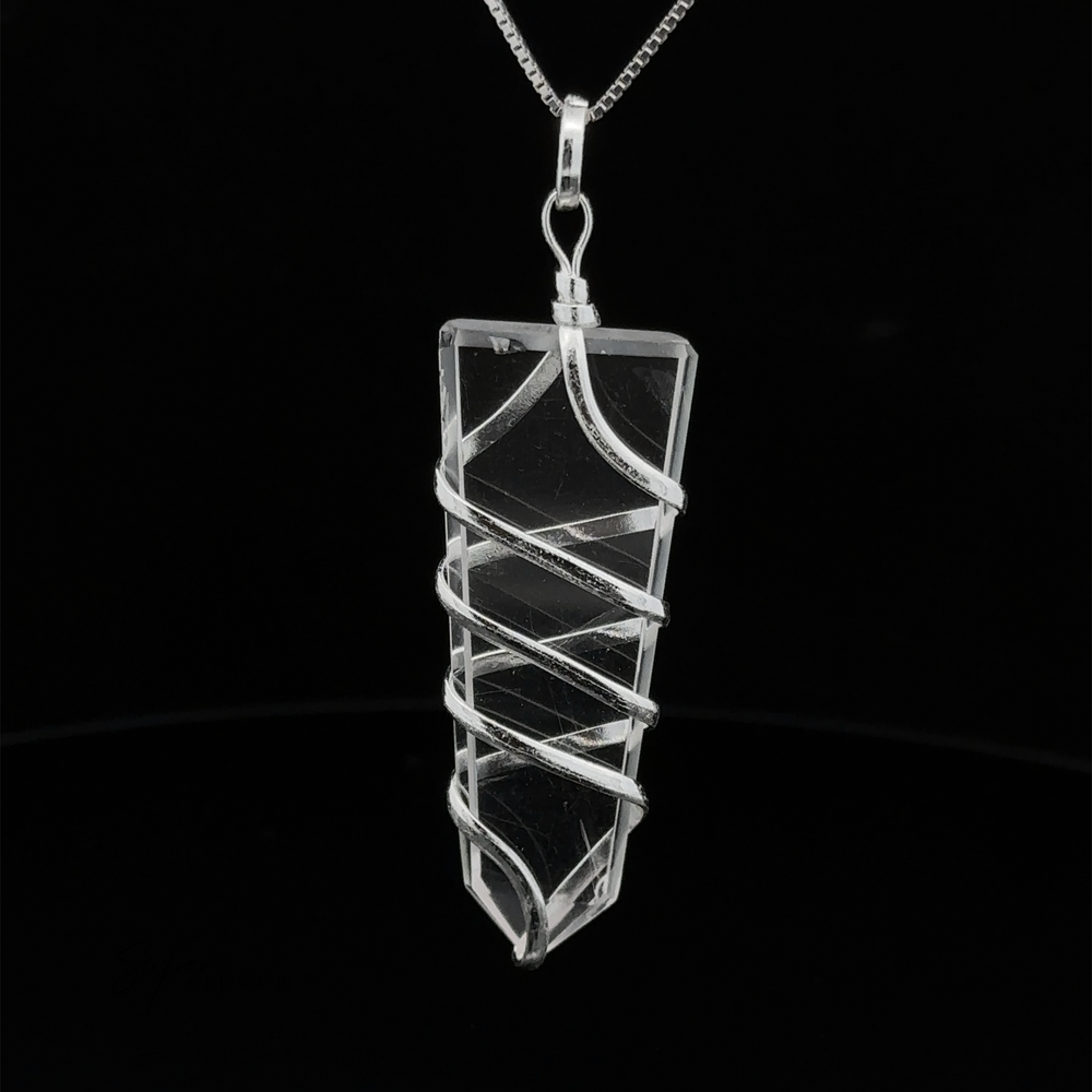 
                  
                    A Wire Wrapped Slab Pendant in spiraled silver wire hangs from a thin silver chain against a black background, epitomizing exquisite gemstone jewelry.
                  
                