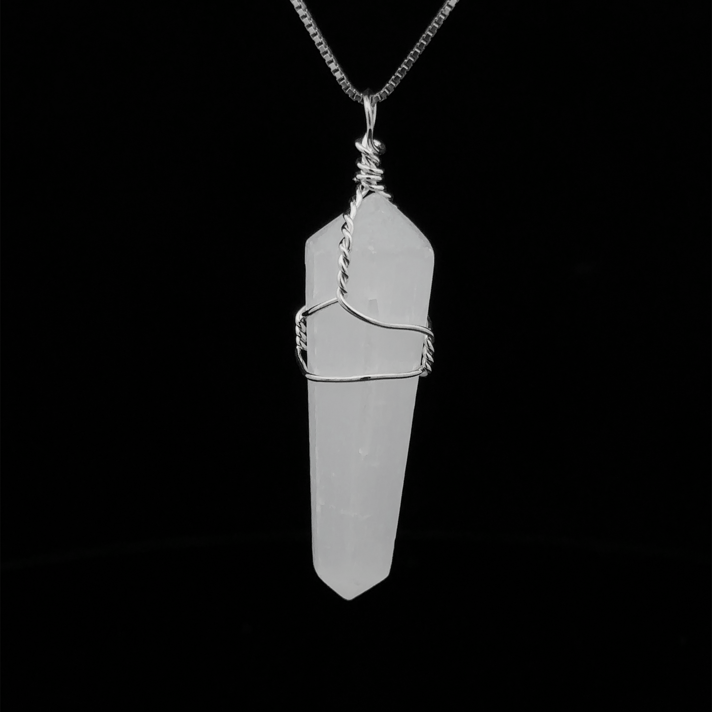 
                  
                    A Wire Wrapped Stone Pendant hangs from a thin silver chain against a black background, reminiscent of polished selenite.
                  
                