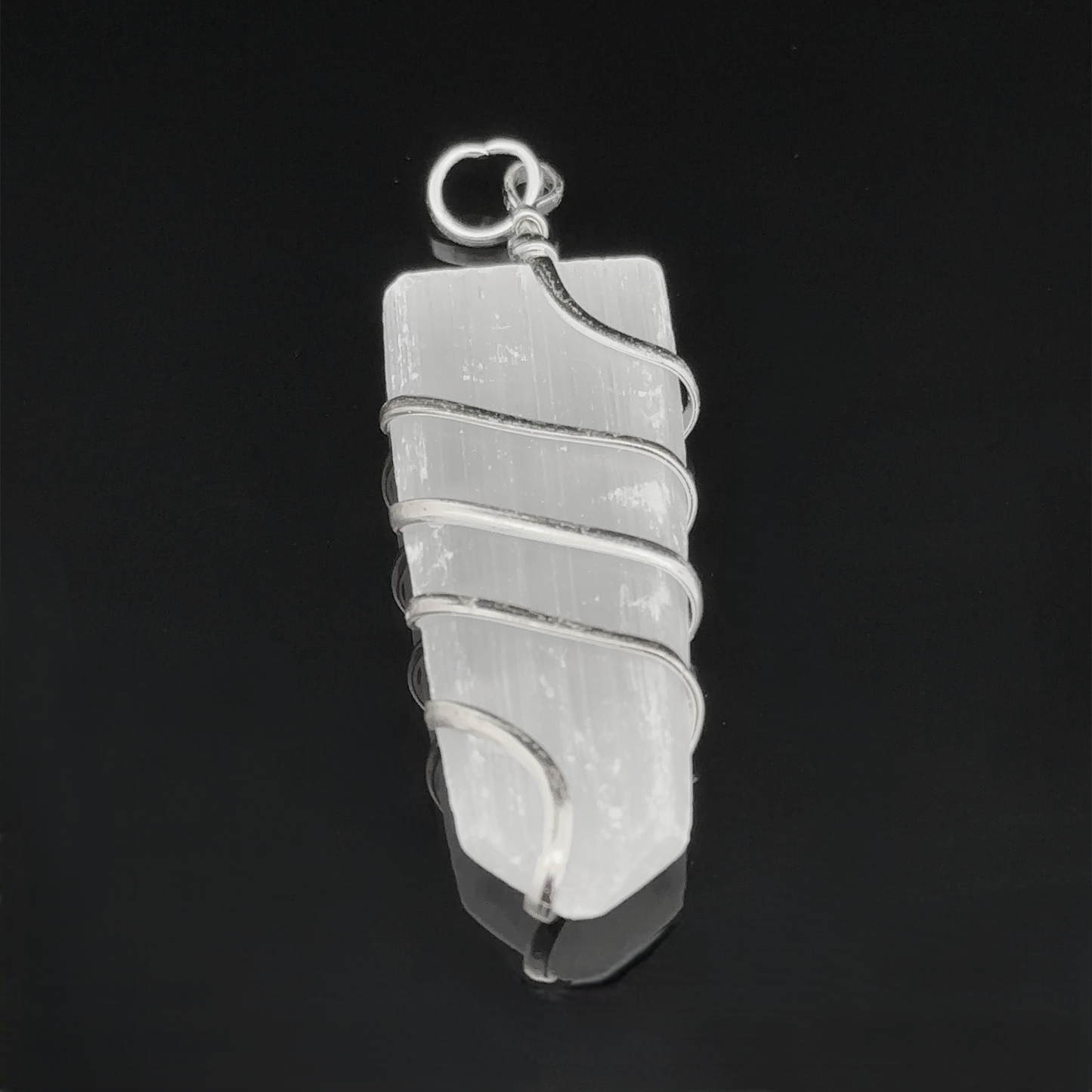 
                  
                    A Wire Wrapped Slab Pendant, elegantly wire wrapped in silver, glimmers against the black background.
                  
                