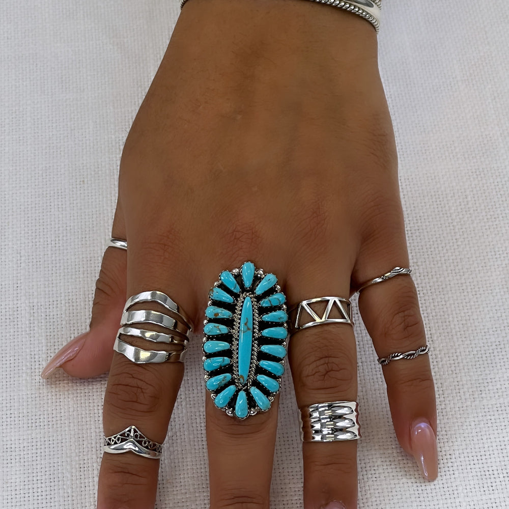 
                  
                    A woman's hand with the Open Shield Band, featuring turquoise and silver set on a wide tapered band made of .925 sterling silver.
                  
                
