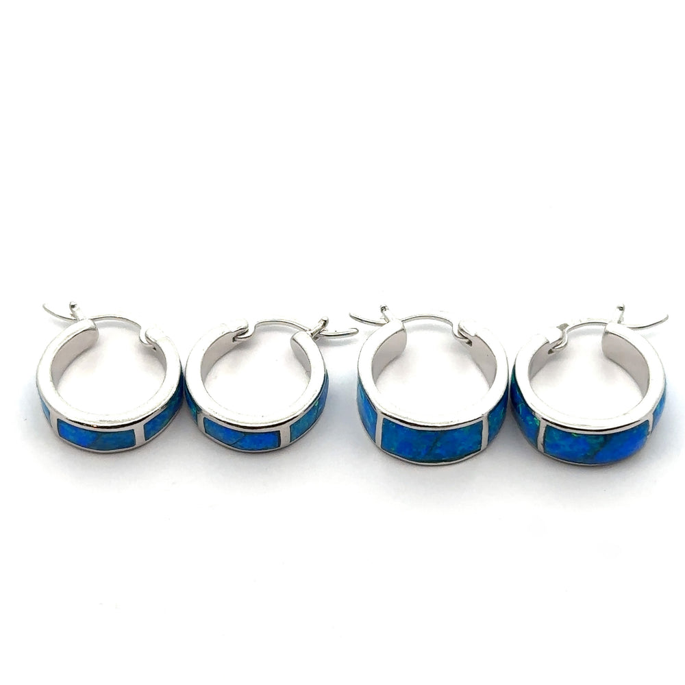 Four Blue Lab-Created Opal Huggie Hoop Earrings with a rhodium finish are arranged in a row on a white background.