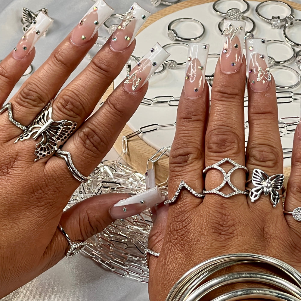 
                  
                    Two hands with elaborate manicured nails display multiple .925 Sterling Silver rings. In the background, a Pave Set Cubic Zirconia Chevron Ring is arranged on a display stand.
                  
                