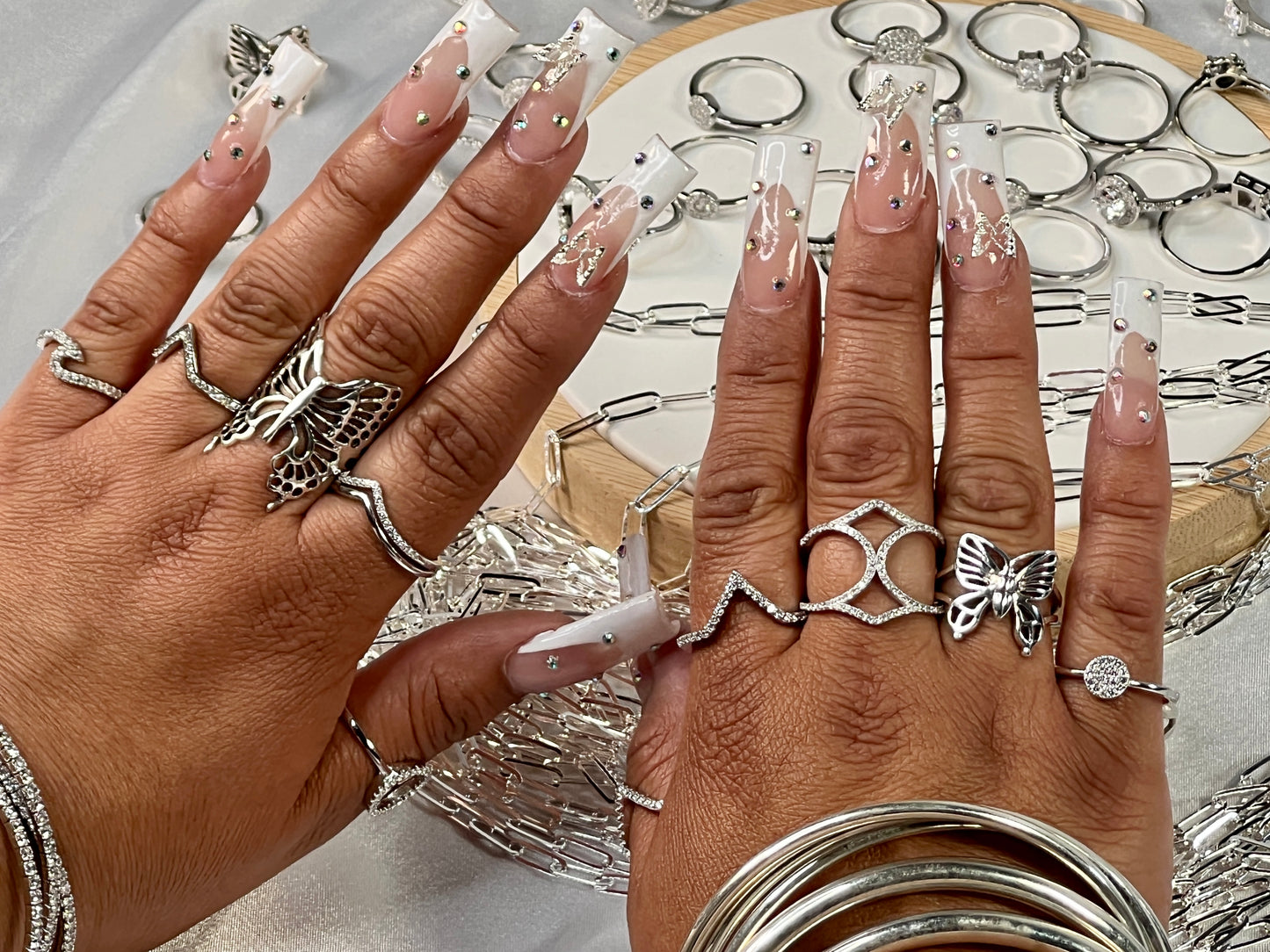 
                  
                    Two hands with elaborate manicured nails display multiple .925 Sterling Silver rings. In the background, a Pave Set Cubic Zirconia Chevron Ring is arranged on a display stand.
                  
                